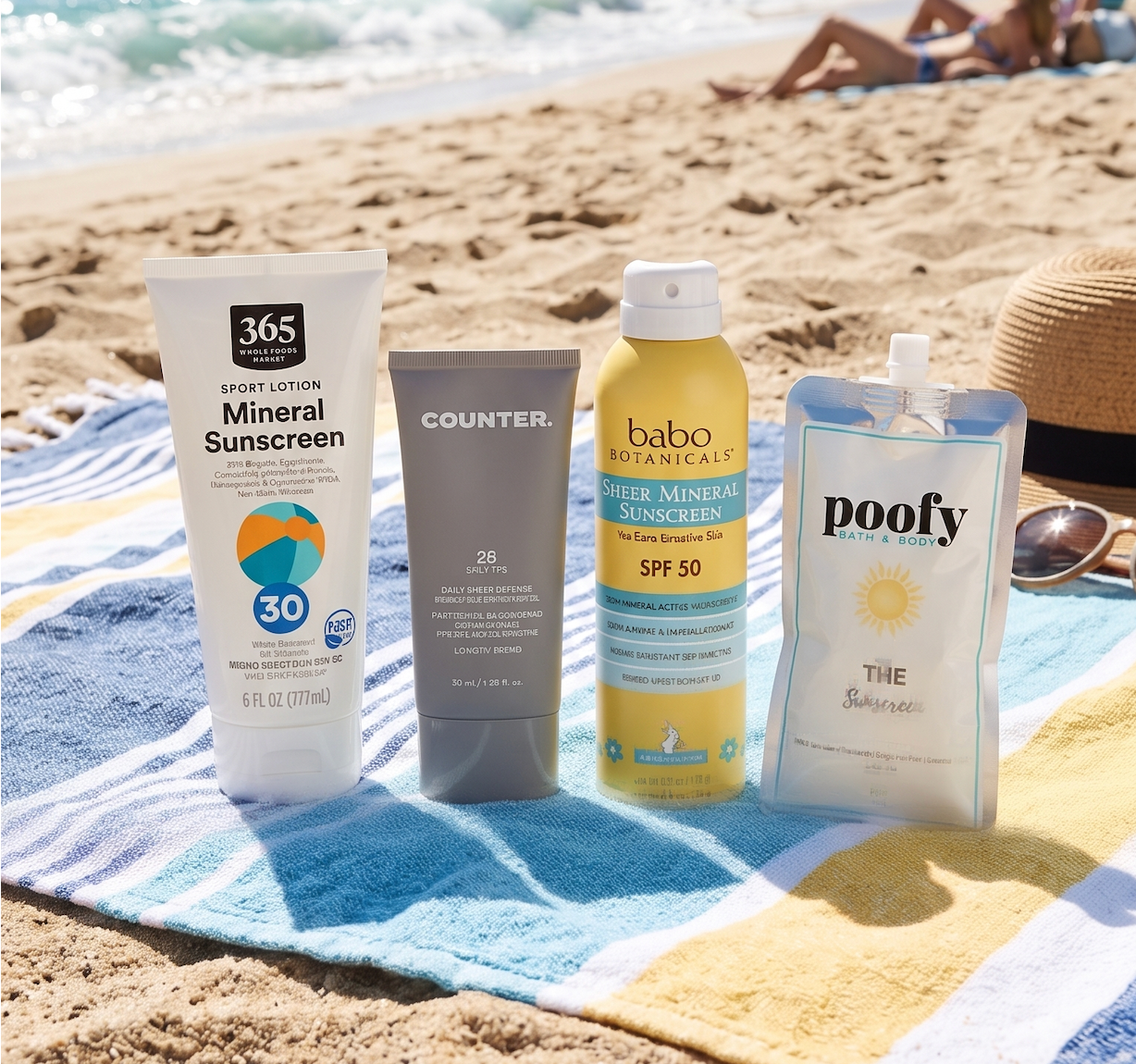 Four sunscreen products, including 365 Mineral Sunscreen, a Counter tube, Babo Botanicals spray, and a Poofy pouch, sitting together on a blue and yellow striped beach towel with the ocean in the background.