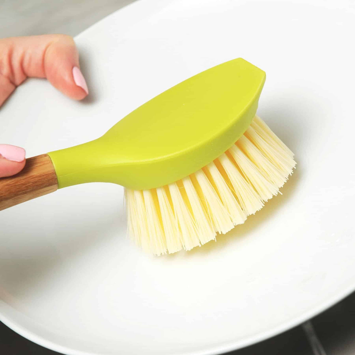 Eco-friendly dishwashing brush cleaning a white plate.