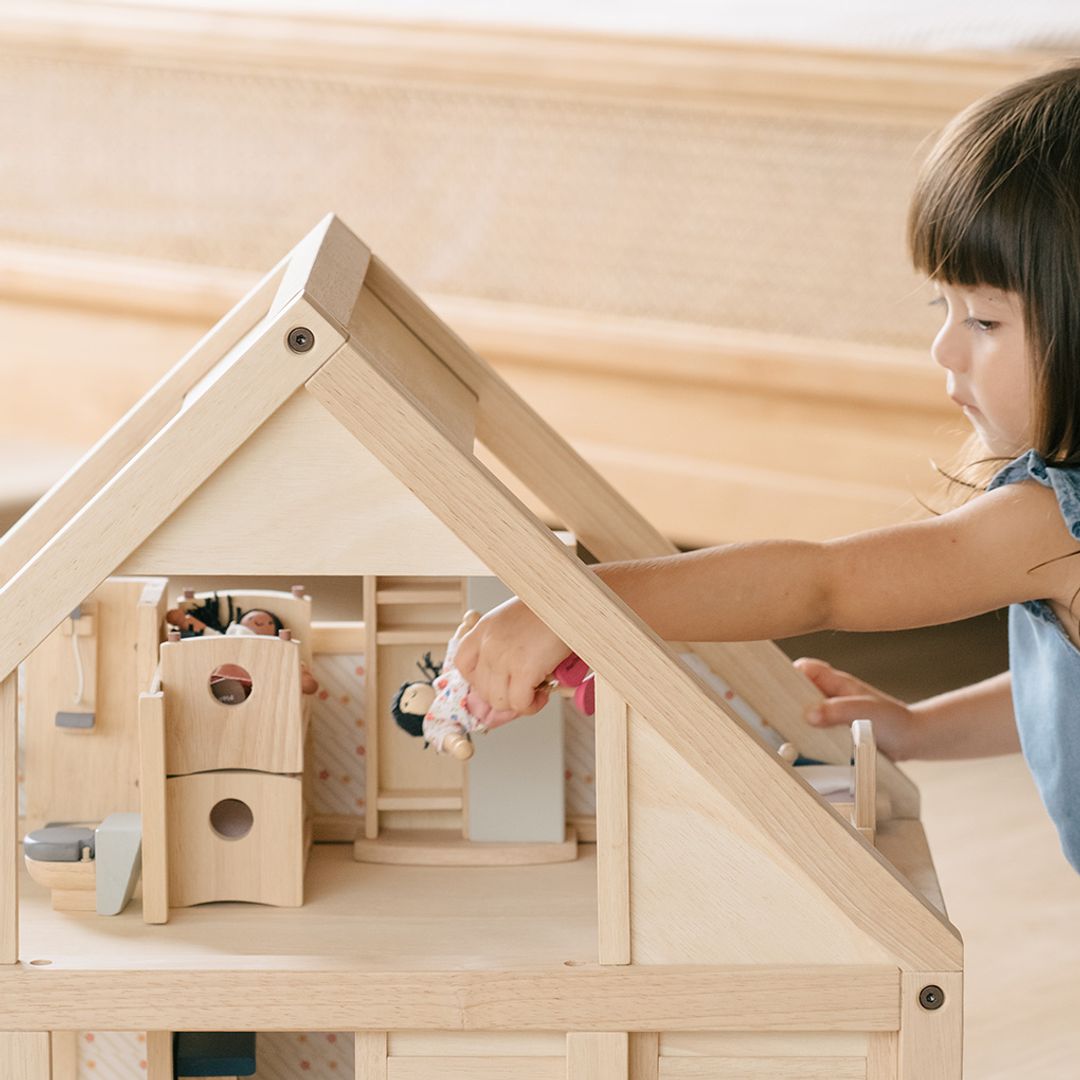 Child playing with a wooden dollhouse, arranging furniture and toys inside.