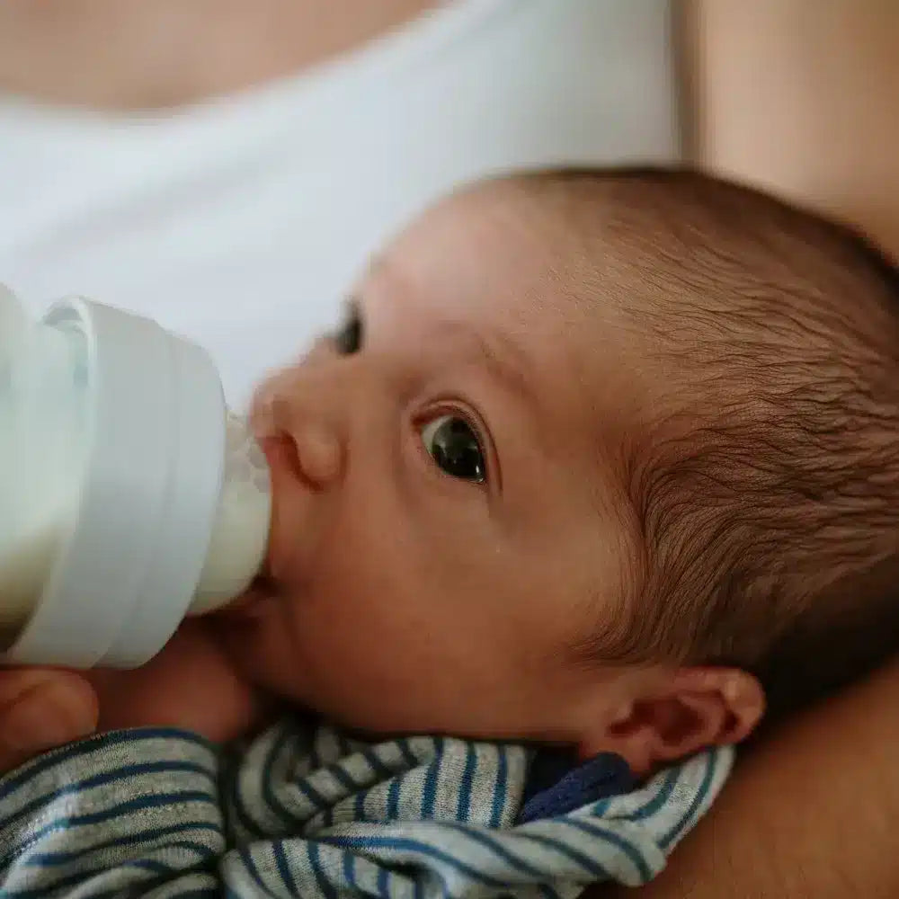 Close-up of a baby drinking from a bottle while being held in a caregiver's arms, representing safe and nurturing bottle-feeding.