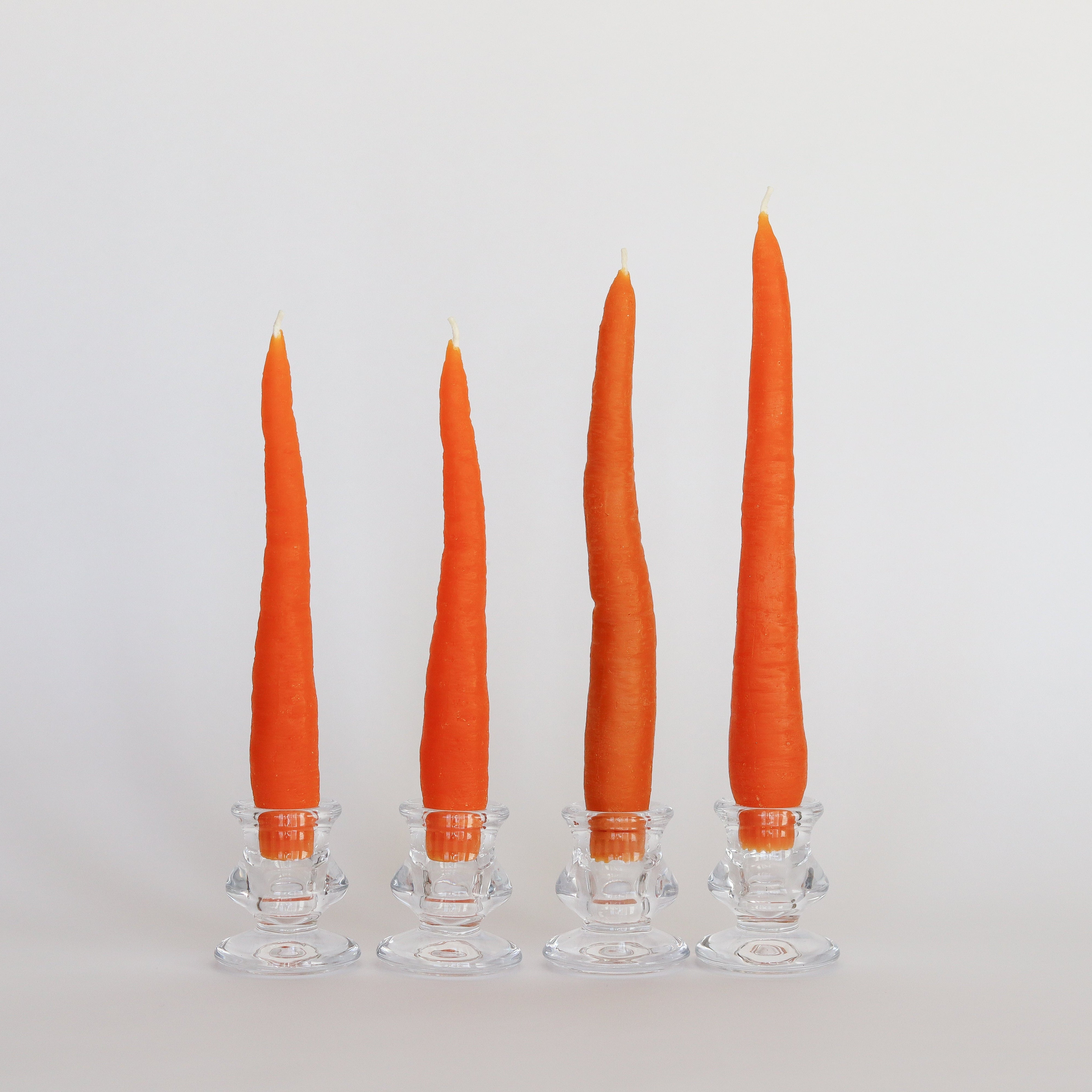 Four orange candles in clear candle holders on a light gray background