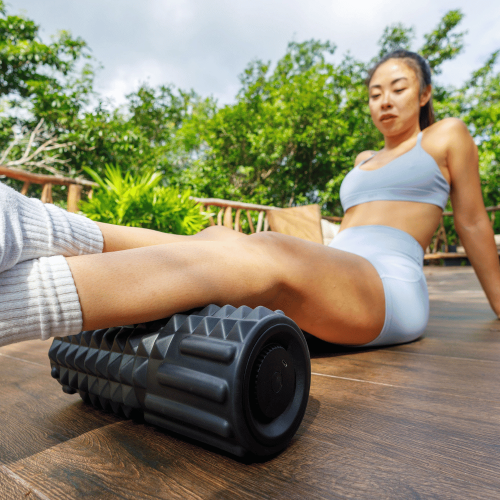 Person using a foam roller outdoors on a wooden surface with greenery in the background