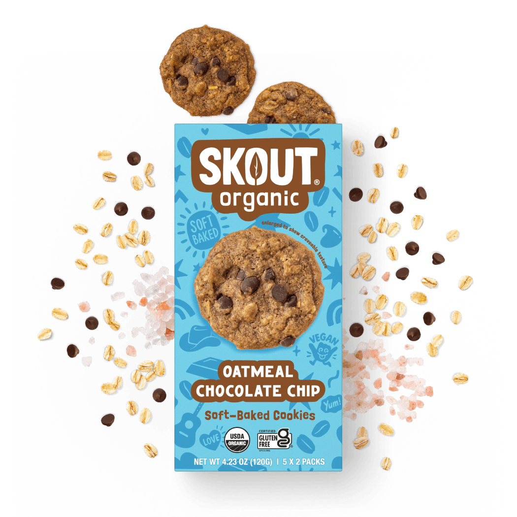 A package of Skout Organic Oatmeal Chocolate Chip cookies is centered on a dark background with scattered oats, chocolate chips, and two cookies above the box.