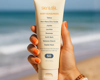 A woman's hand on the beach holding a tube of non toxic sunscreen