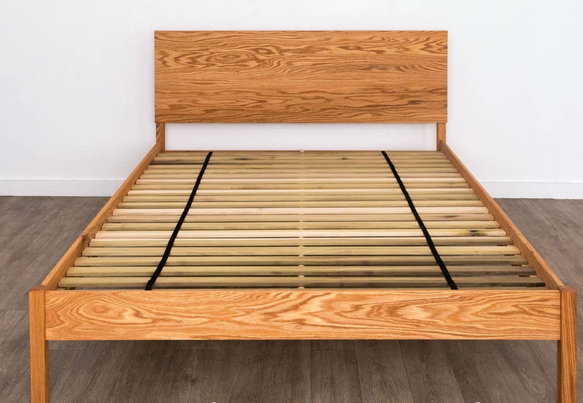 Wooden non-toxic bed frame with simple slatted headboard against a neutral wall.