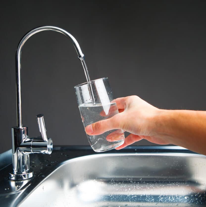 Hand filling a glass with filtered water from a modern kitchen faucet.