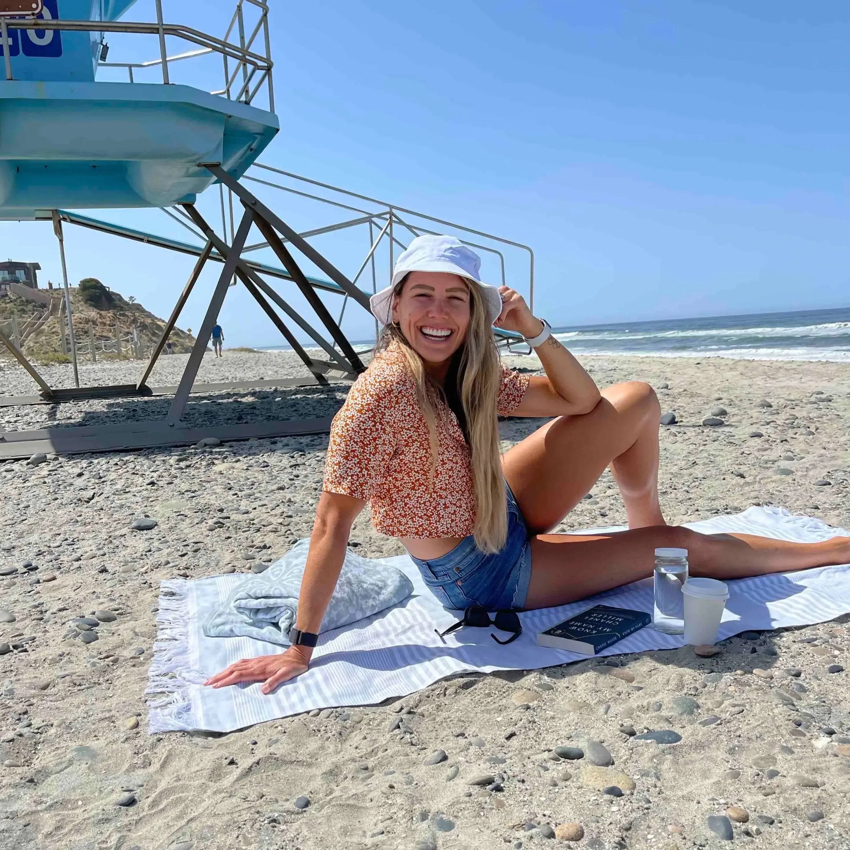 Woman sitting on a towel at the beach with a lifeguard tower in the background