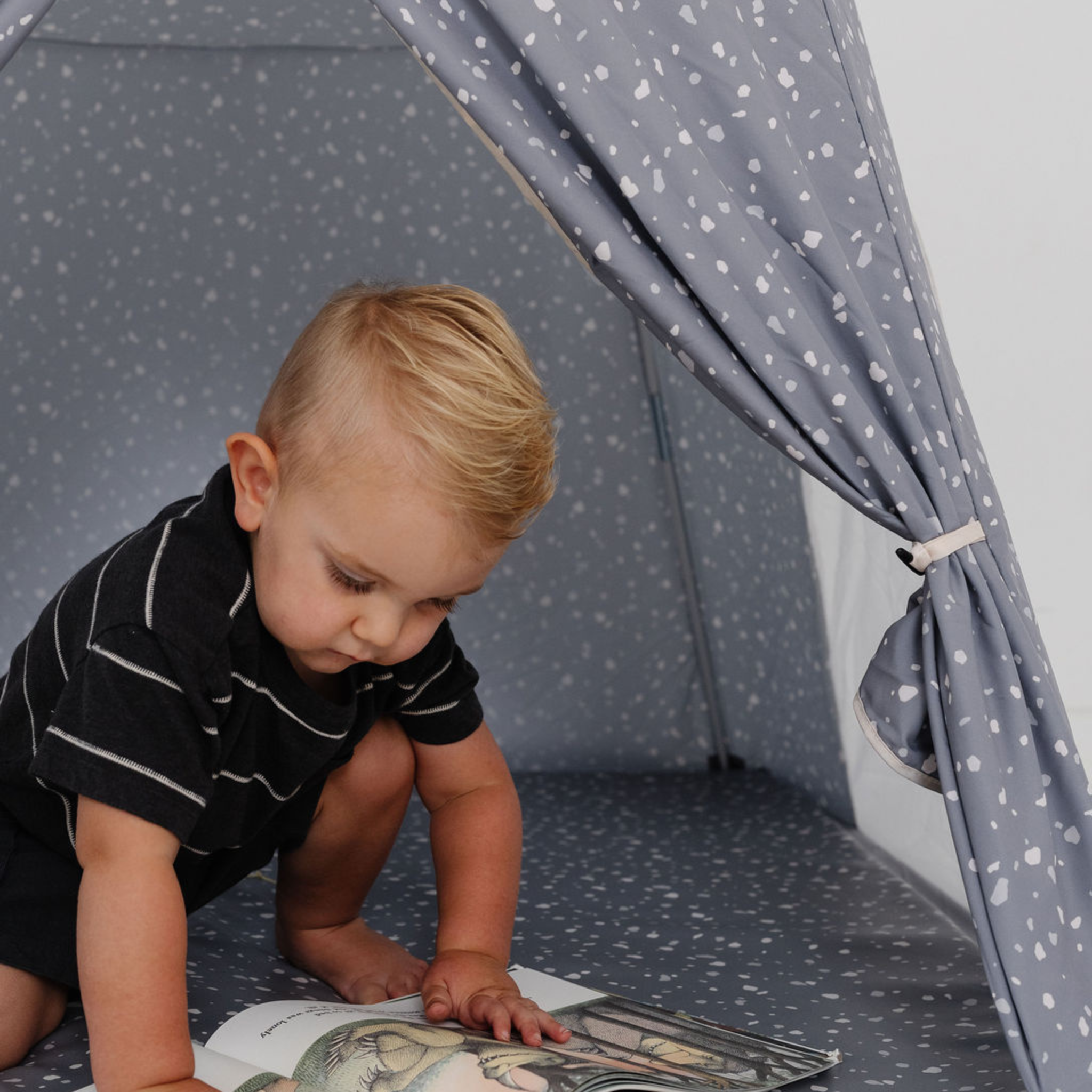 Child playing with a book inside a gray tent with star patterns.