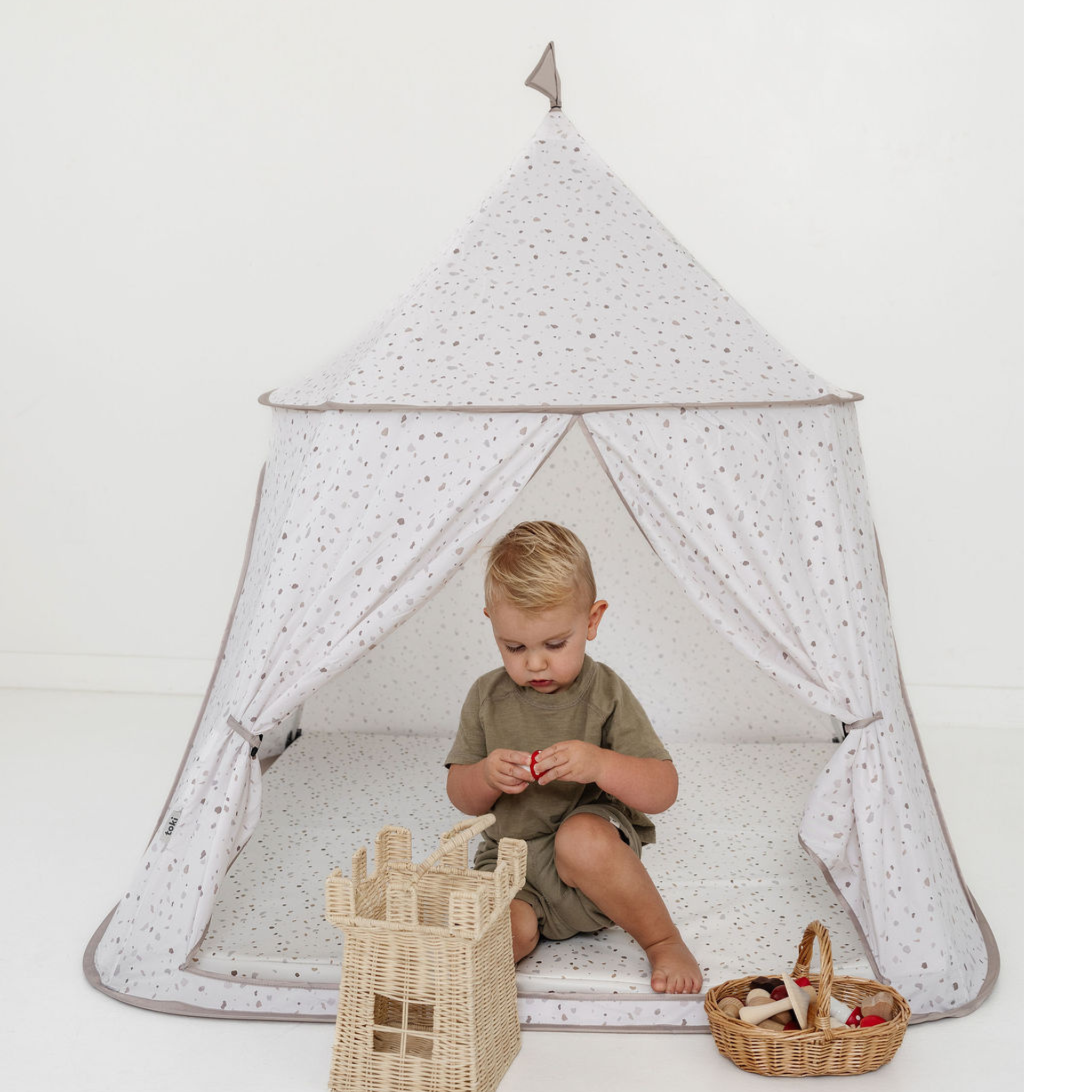 Child sitting inside a star-patterned tent with toys on a white background