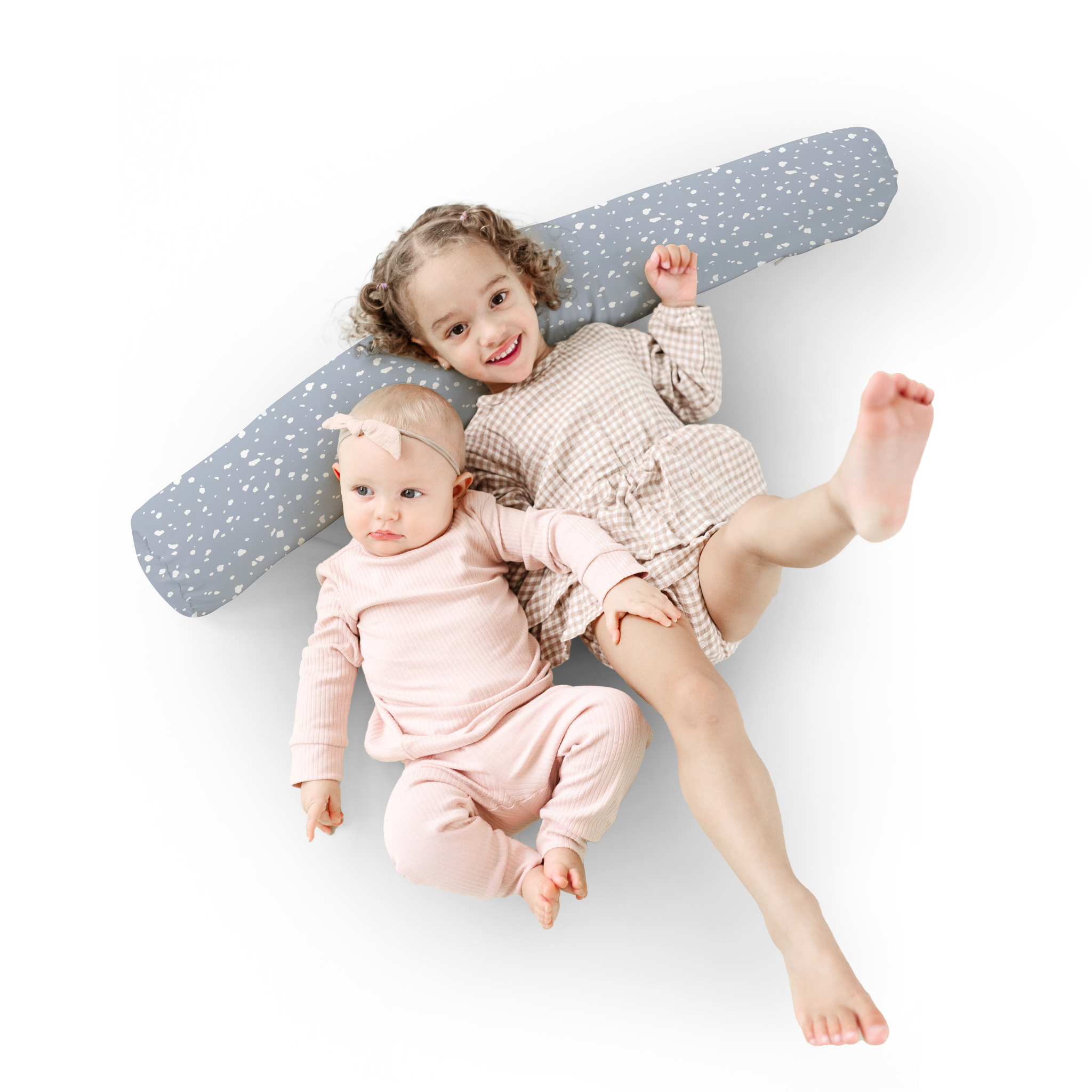 Two children lying on a large gray pillow with white polka dots on a white background