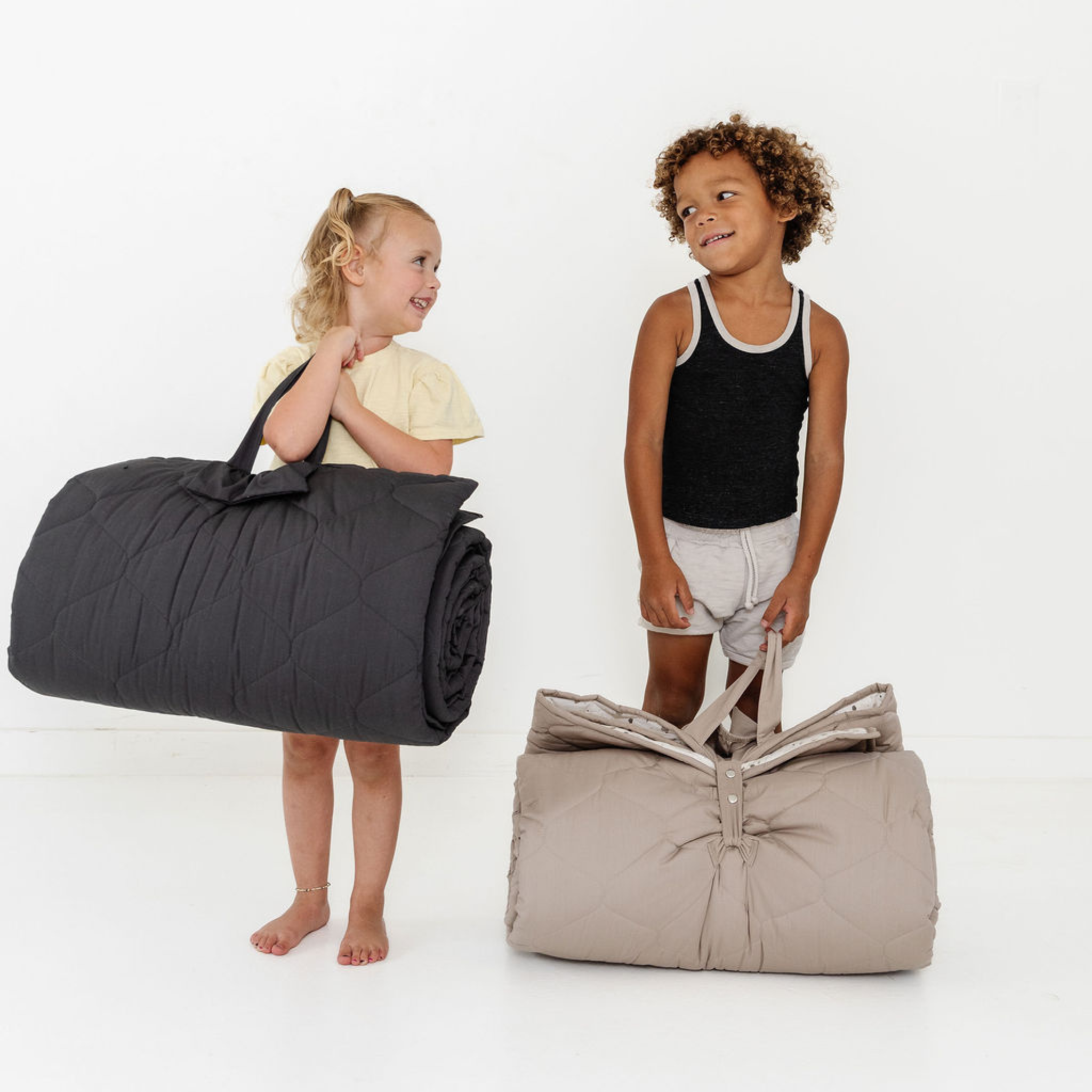 Two children holding rolled-up sleeping bags against a white background