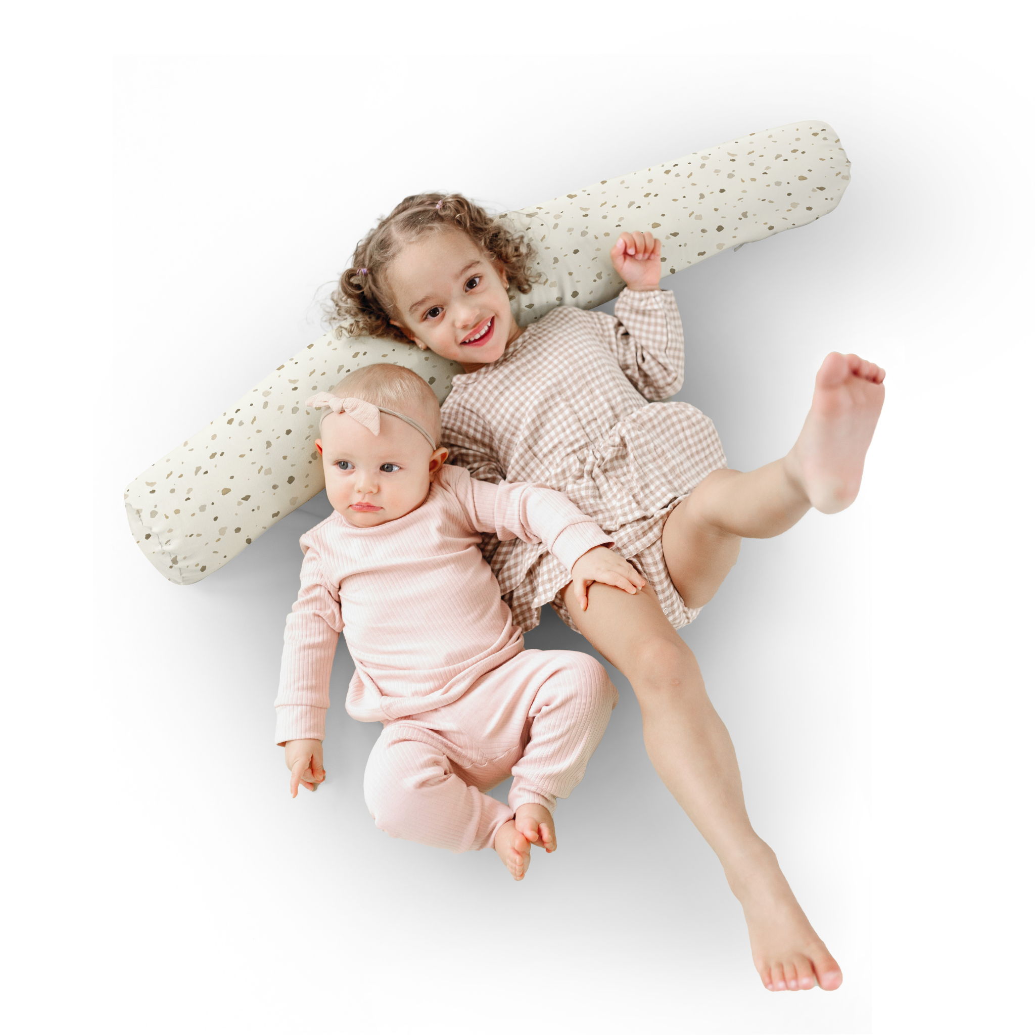 Two children lying on a white surface with a polka dot pillow.