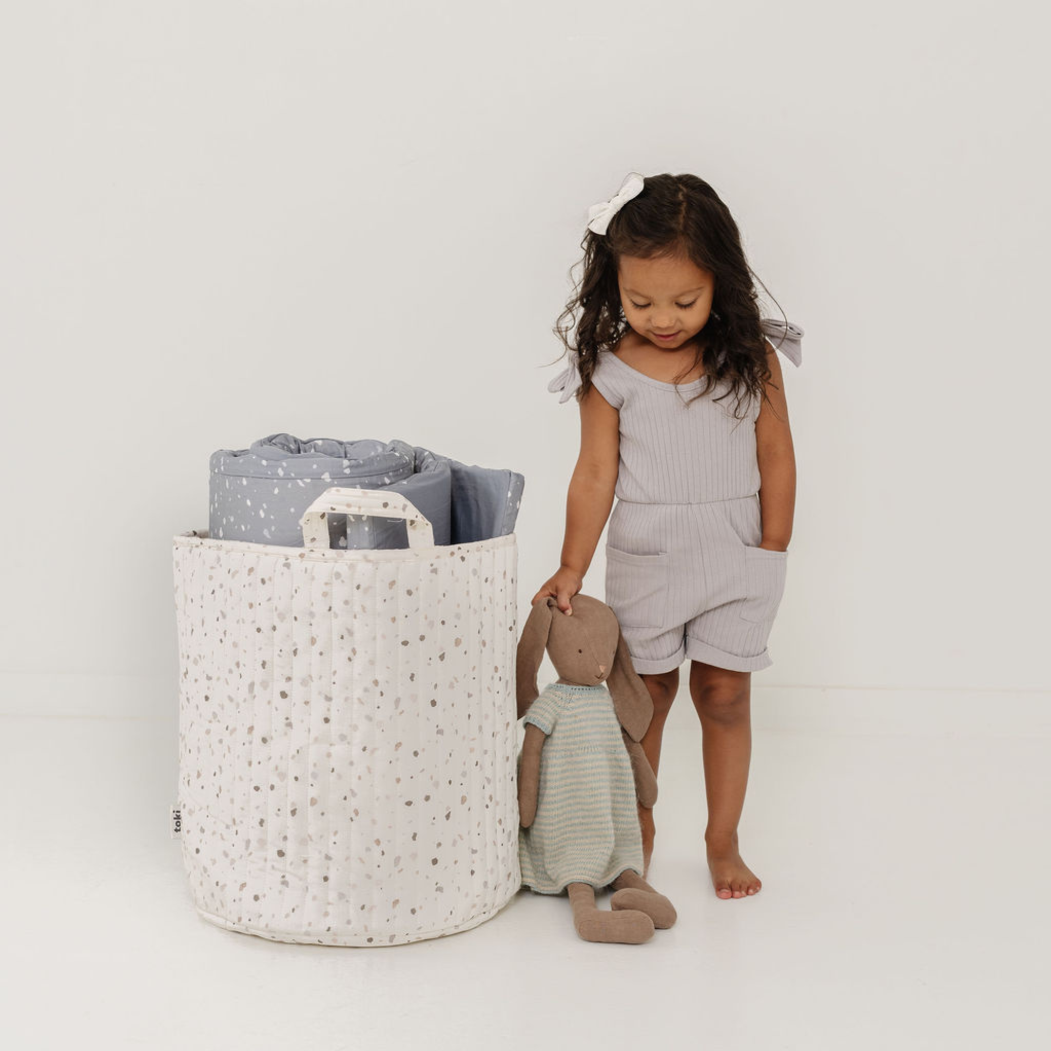 Child playing with a toy next to a laundry basket on a white background