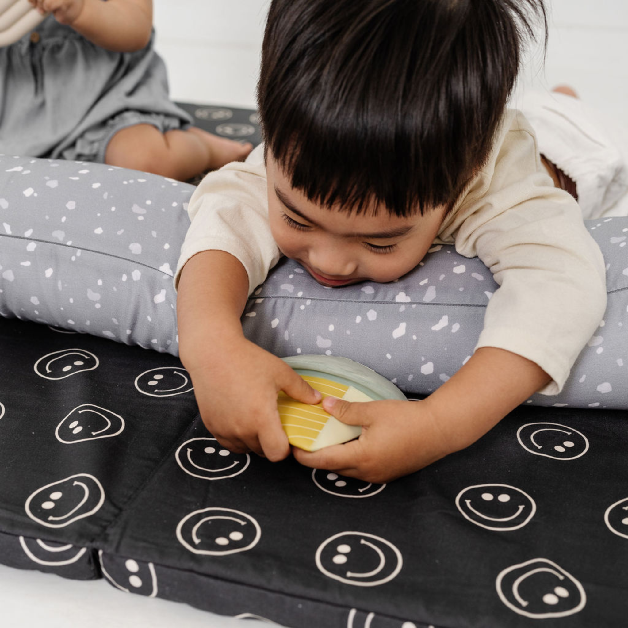 Child playing with a toy on a black mat with smiley face patterns