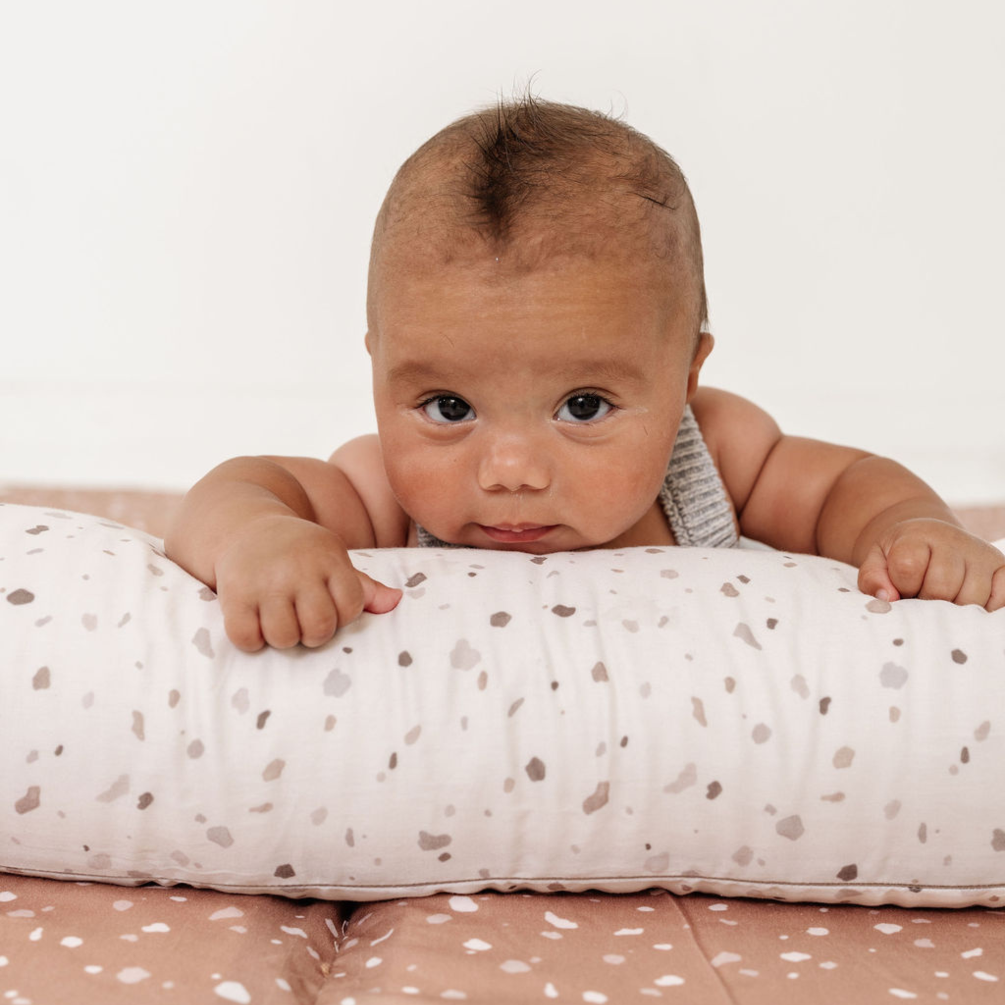 Baby lying on a spotted cushion with a plain background