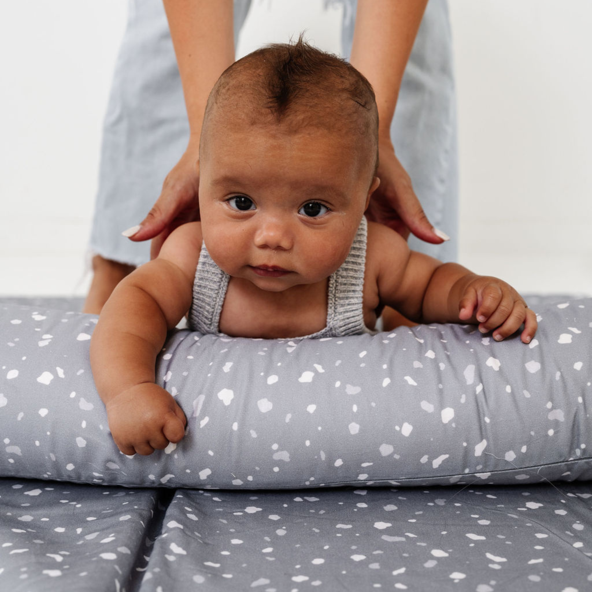 Baby lying on a gray cushion with white heart patterns, being held by an adult.