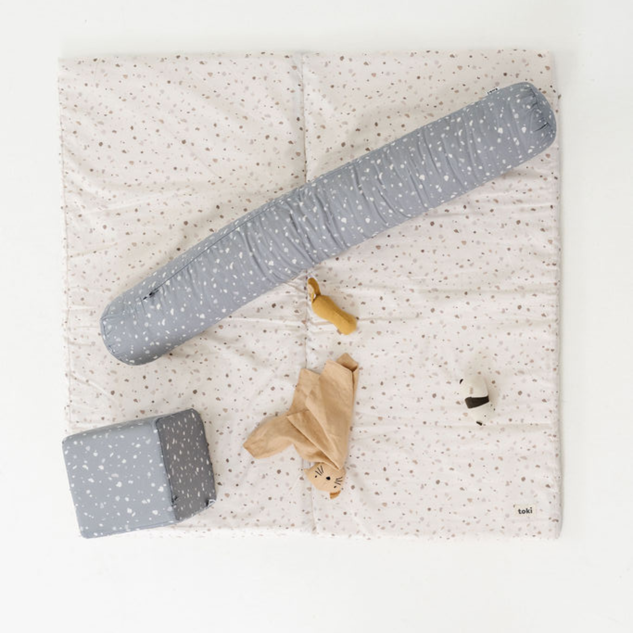 Children's play mat with gray and white polka dot toys on a light speckled background