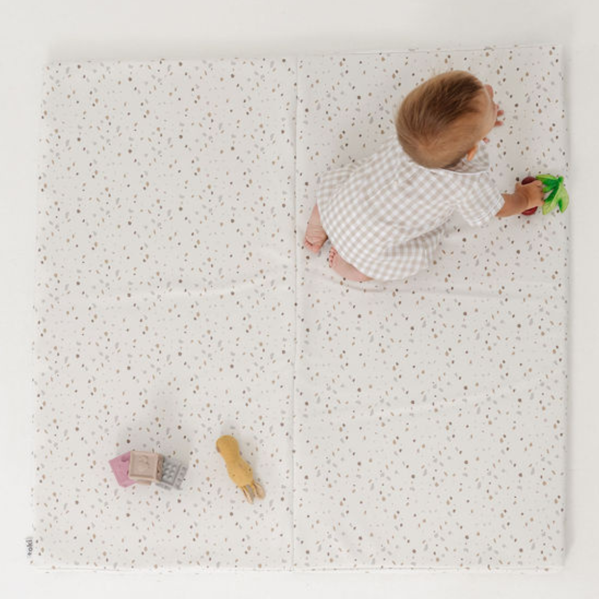 Baby playing on a white play mat with toys scattered around