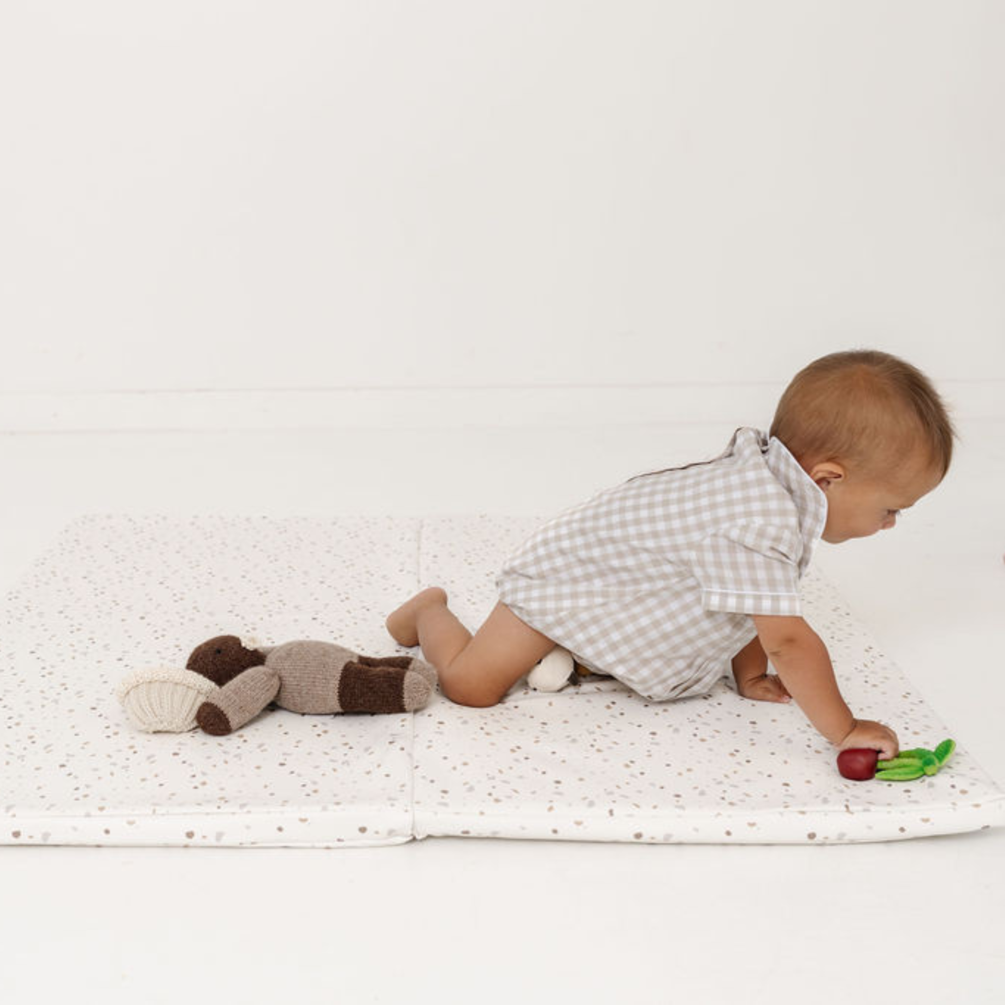 Baby playing on a white blanket with a toy and a stuffed animal.