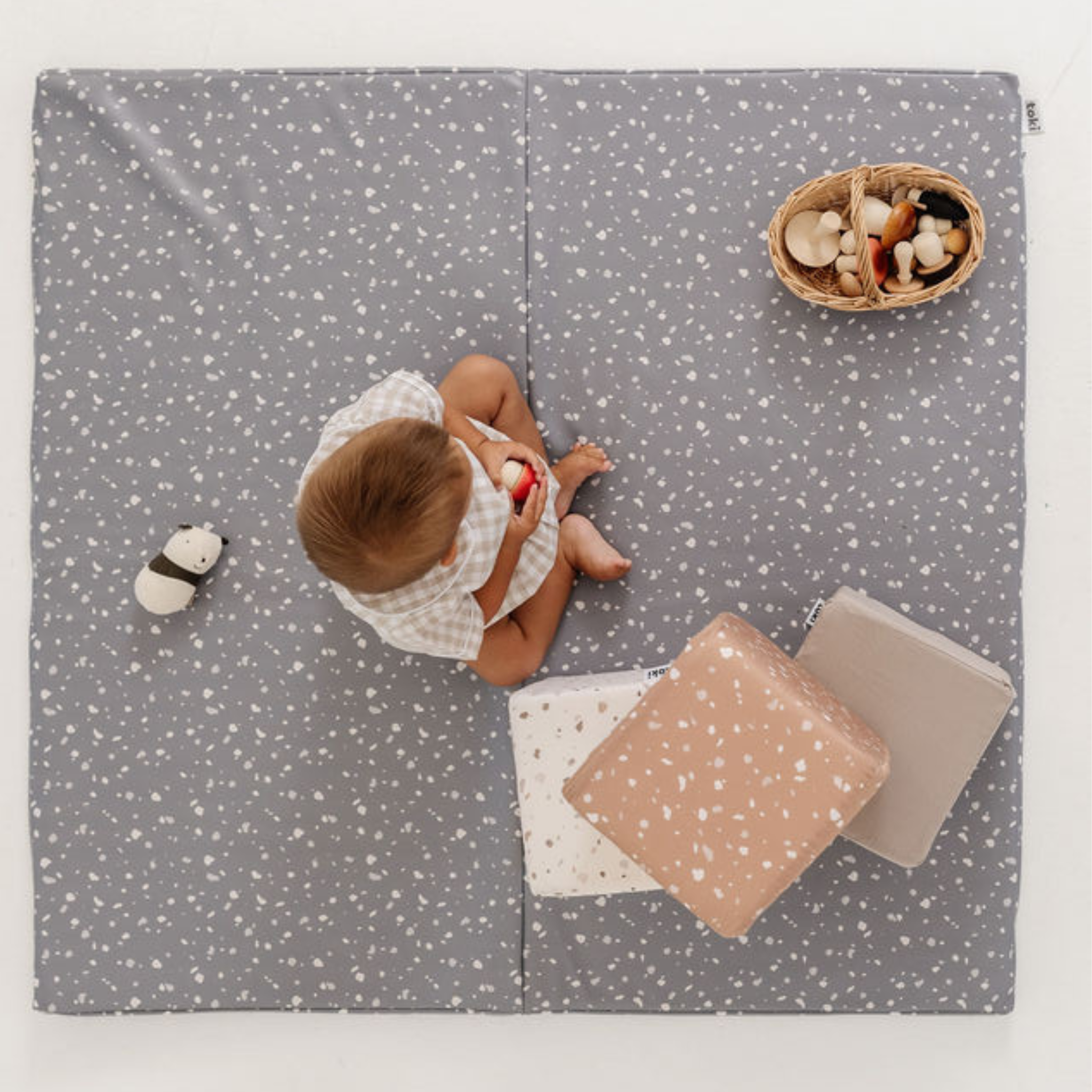 Baby playing on a gray play mat with toys around