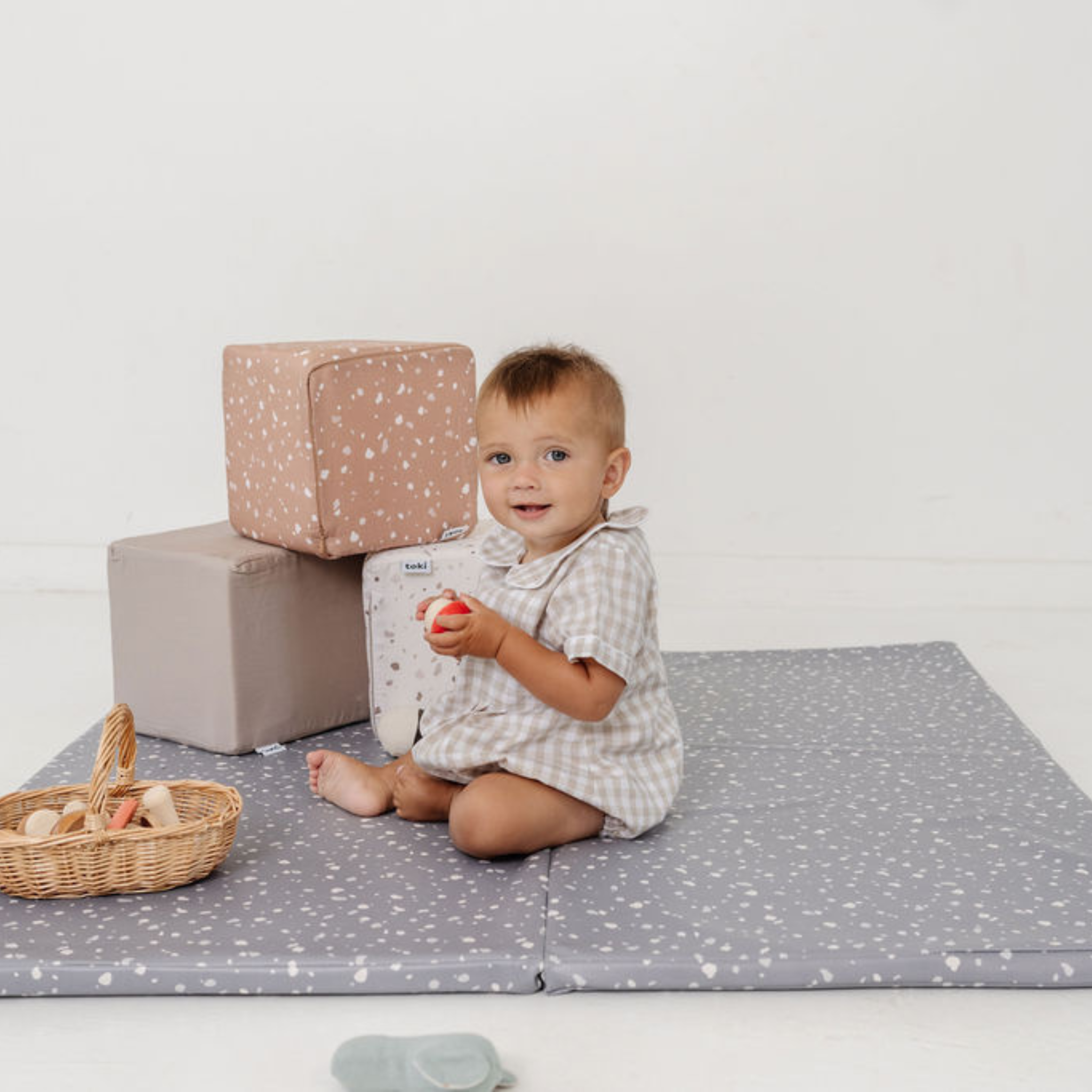 Child sitting on a gray play mat with blocks and toys