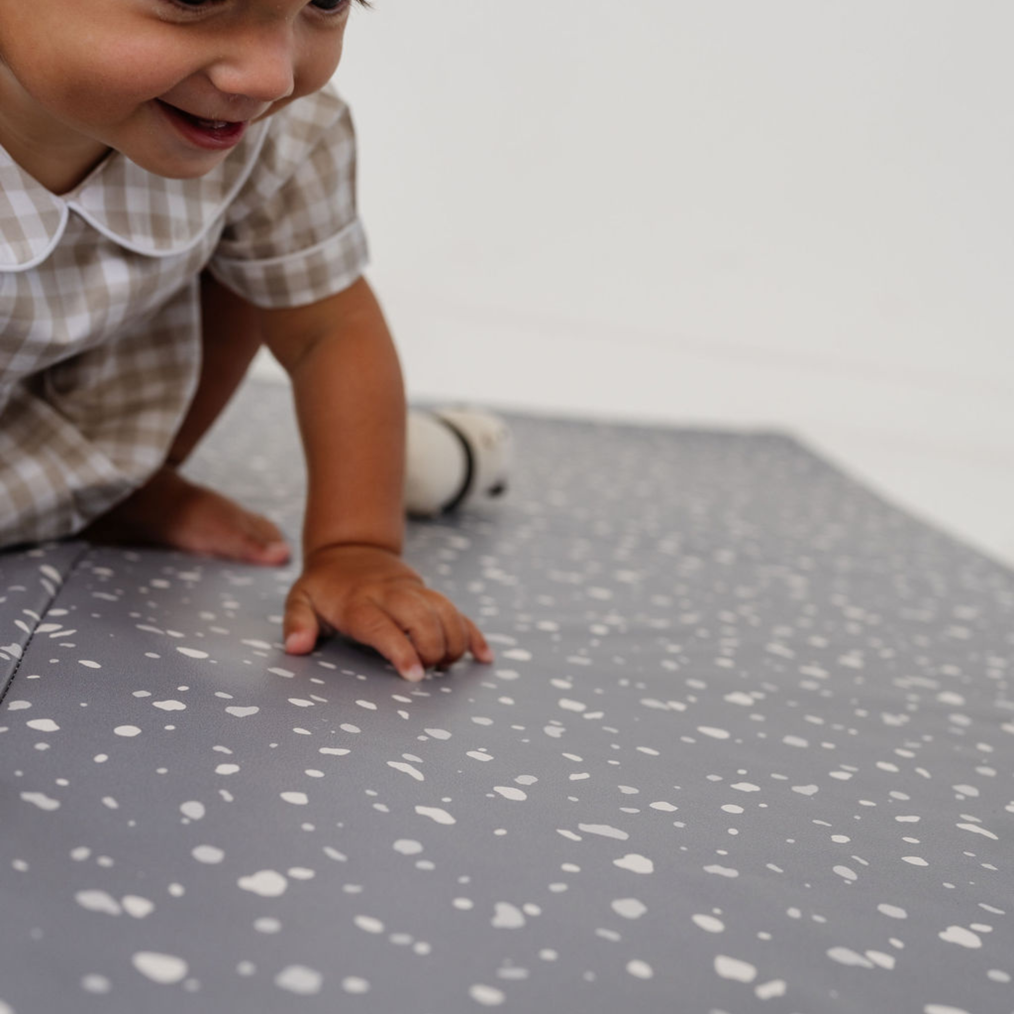 Child playing on a gray play mat with white speckles
