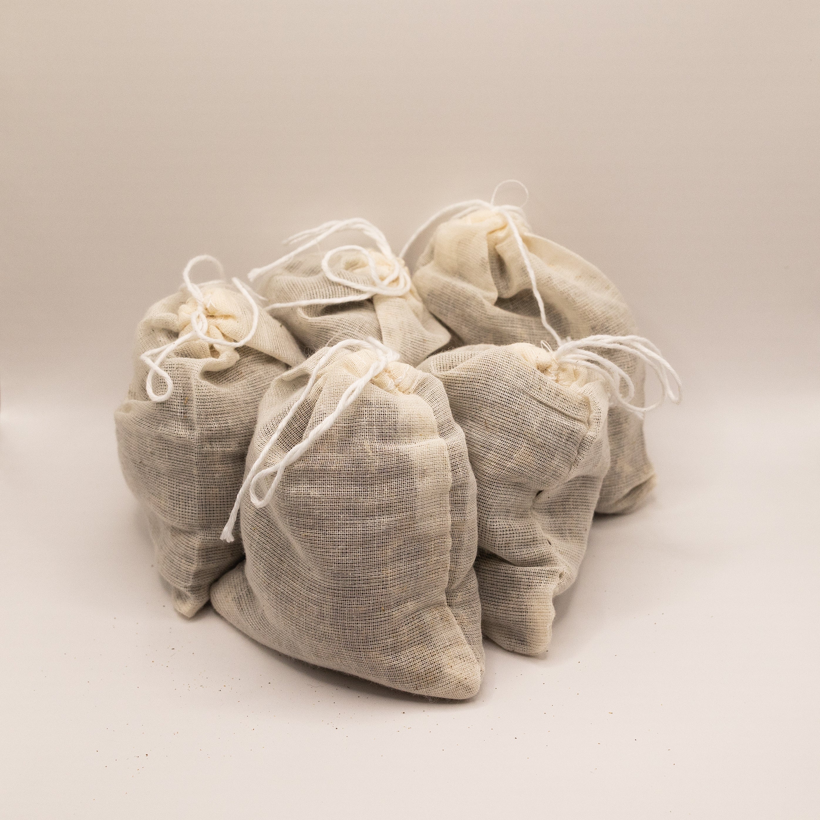 Set of five beige fabric bags with drawstrings on a light beige background