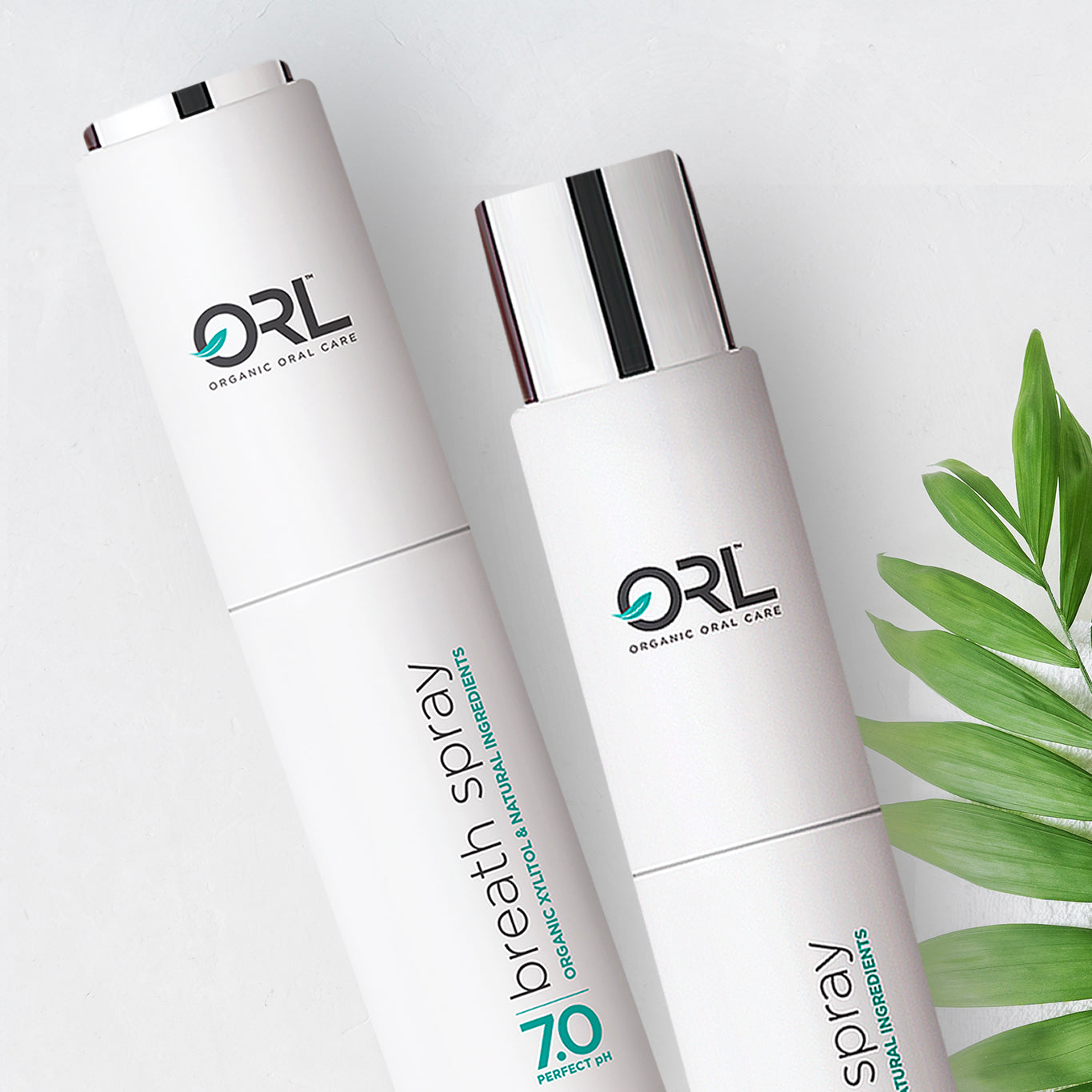 Two ORL Organic Oral Care breath spray bottles on a light background with green leaves.