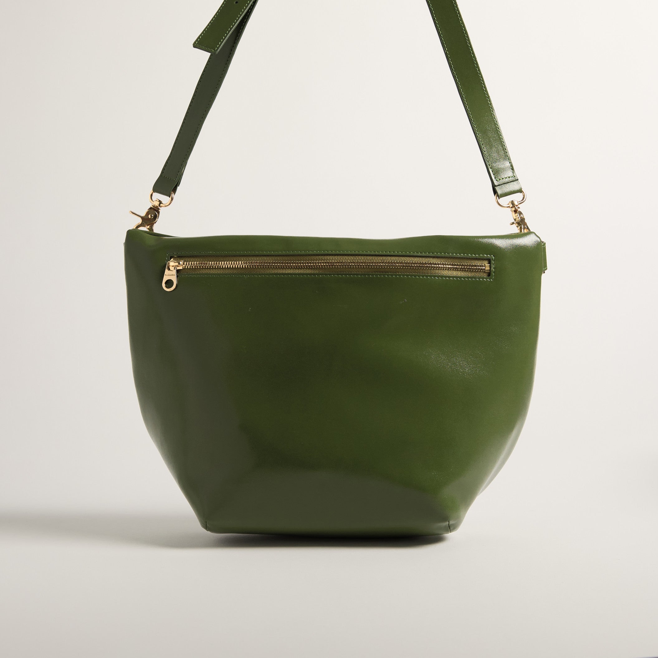 Green leather handbag with a gold zipper on a light gray background