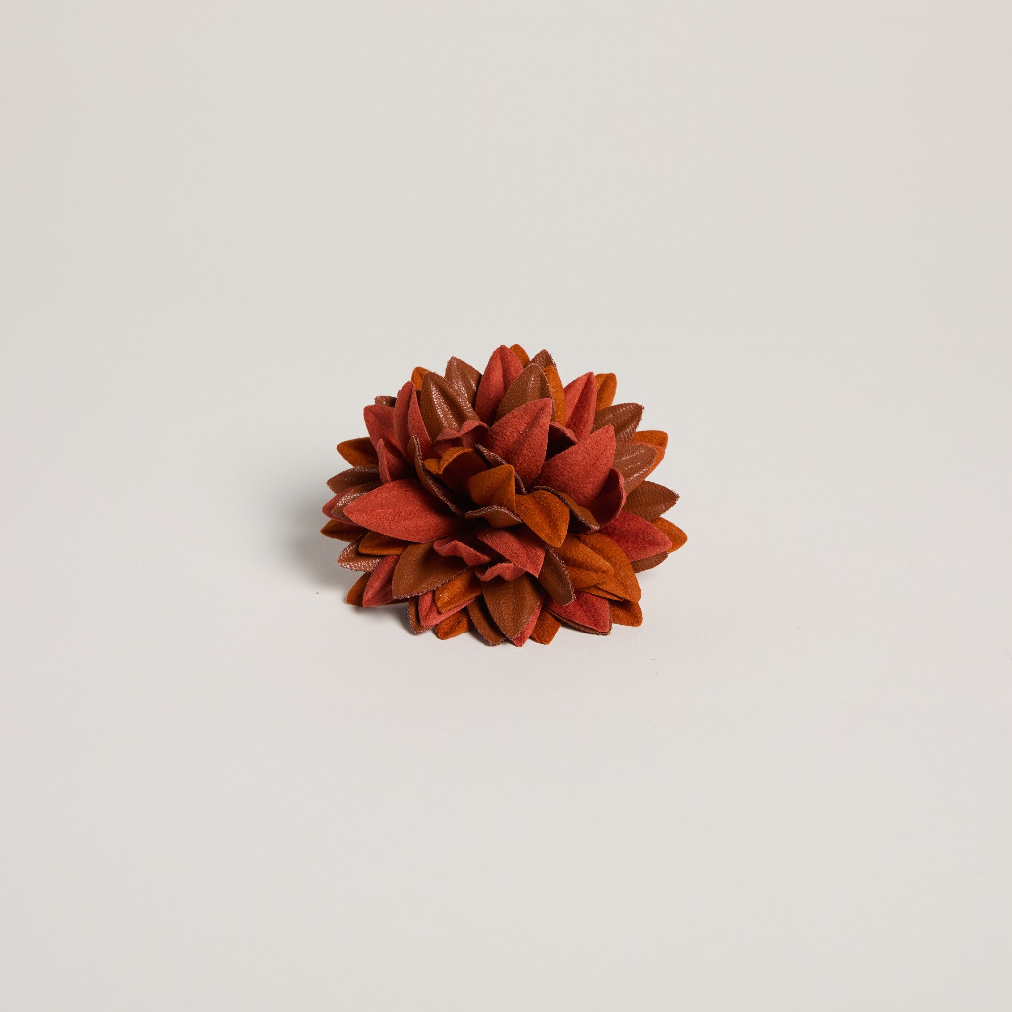 Floral brooch with red and orange hues on a light gray background