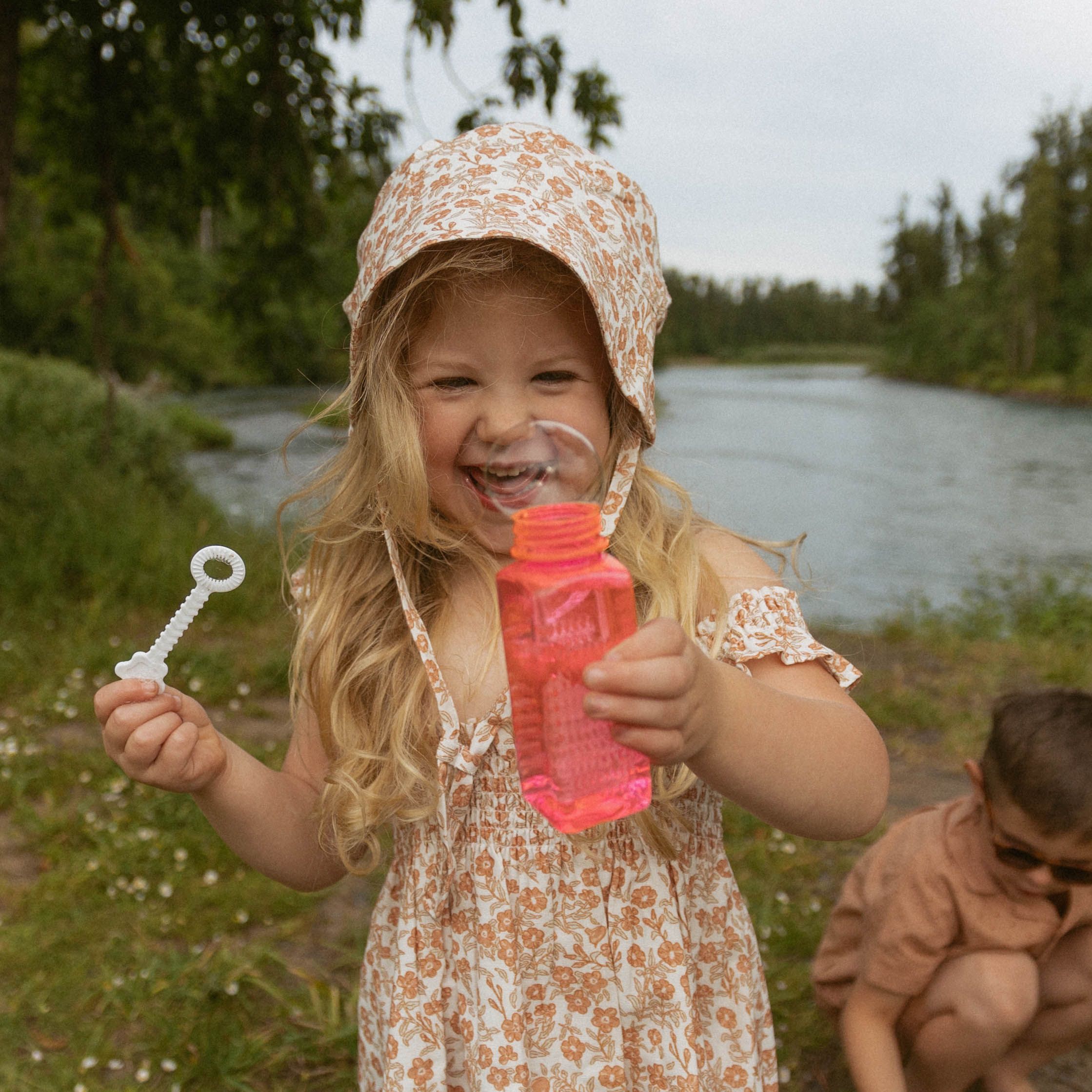Child playing with bubbles outdoors near a body of water