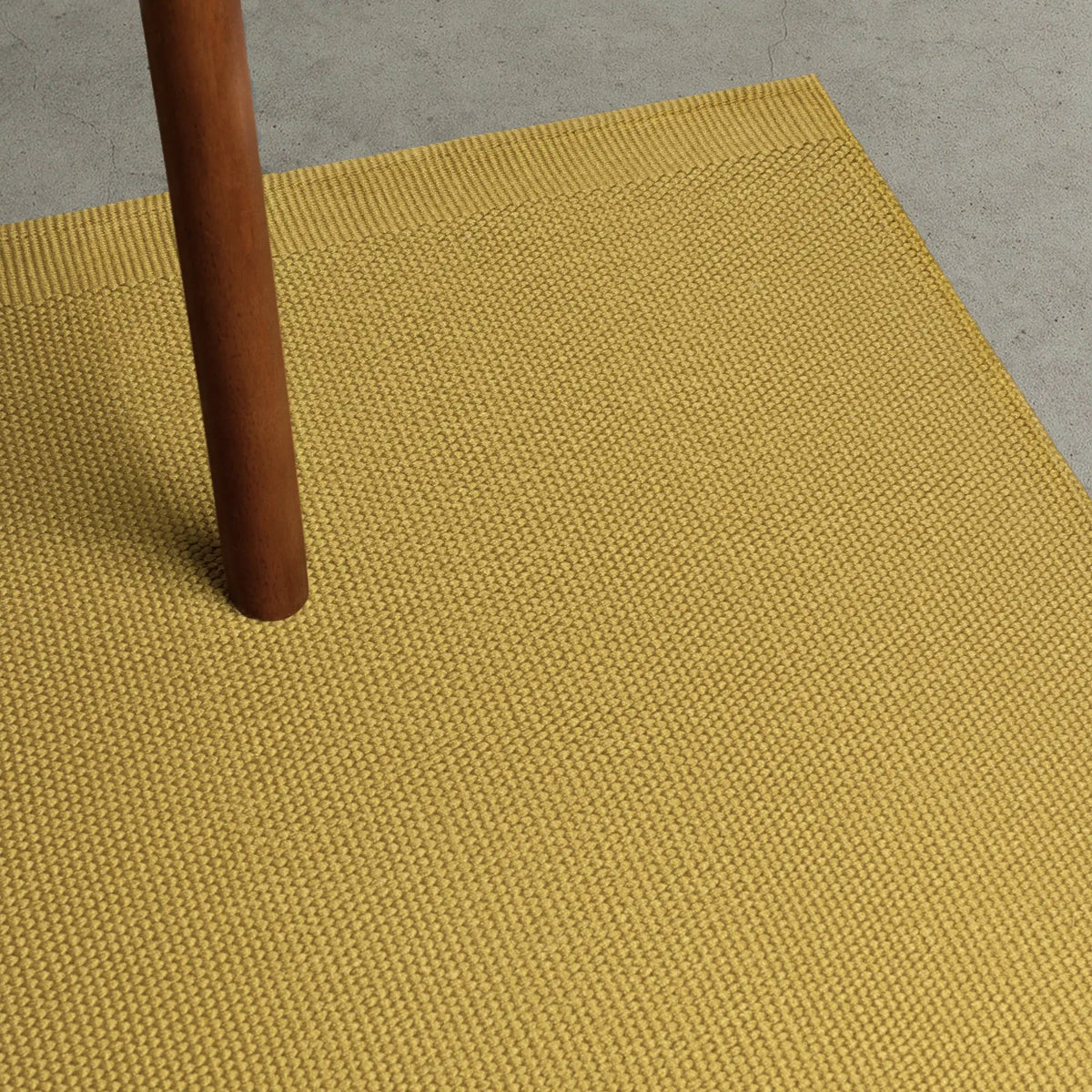Yellow textured rug with a wooden leg partially visible
