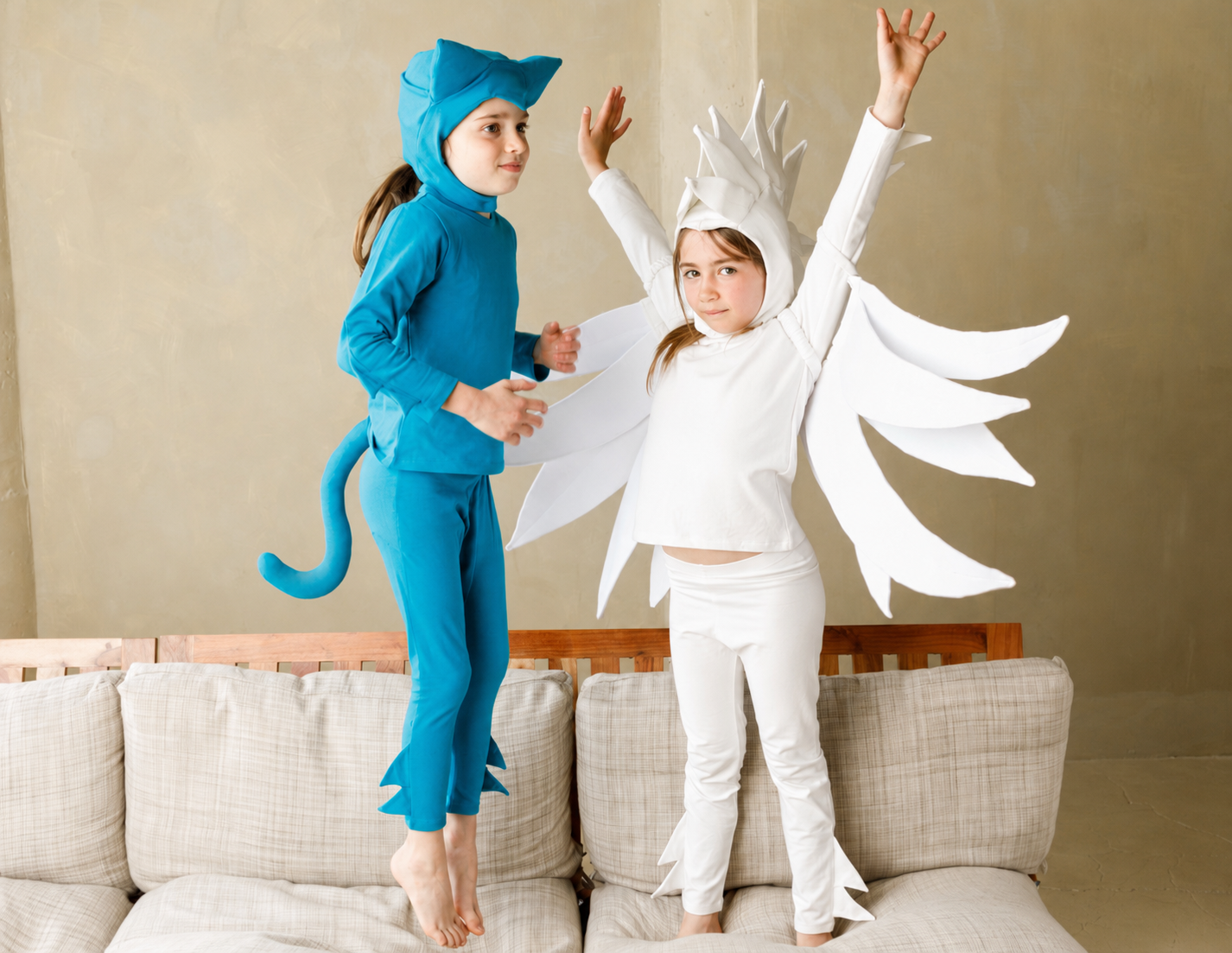 Two children in costume standing on a couch, one in blue and one in white with wings.