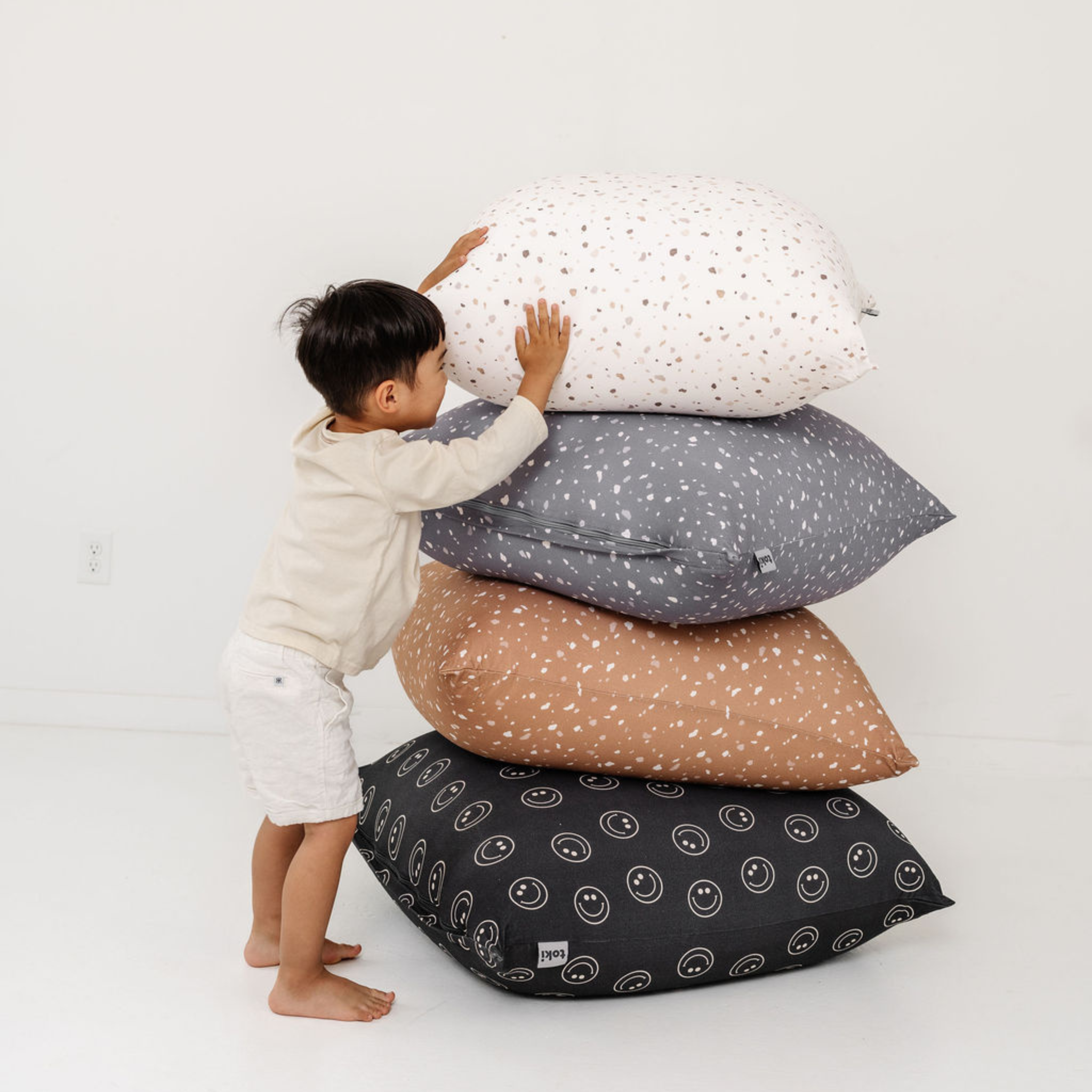 Child playing with a stack of patterned pillows on a white background