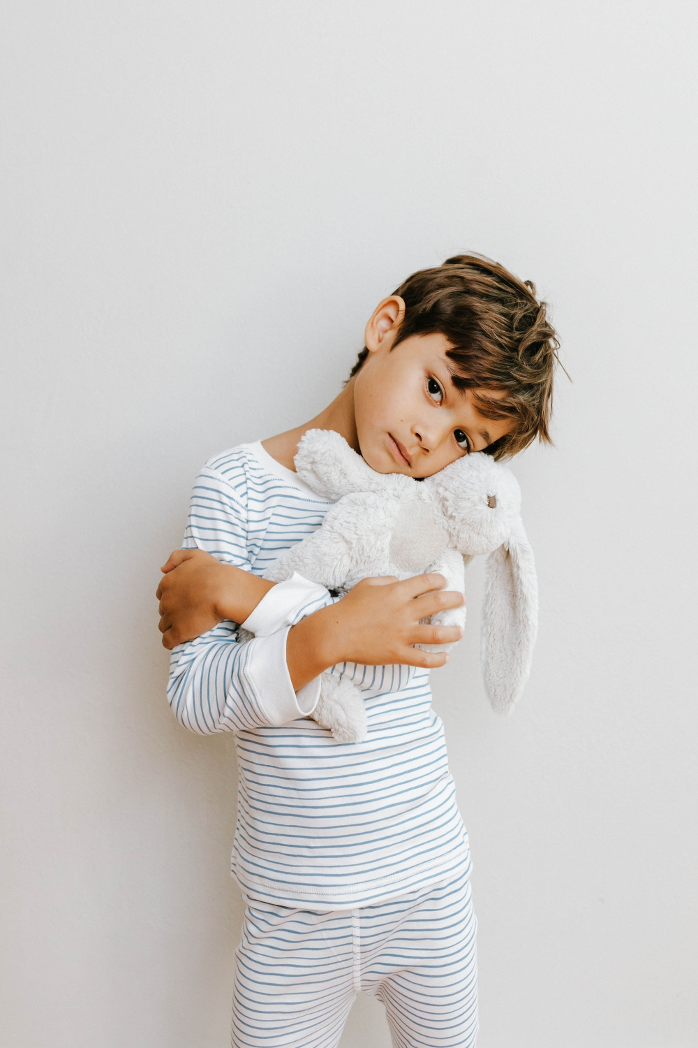 Child wearing a striped outfit holding a white bunny toy against a plain background
