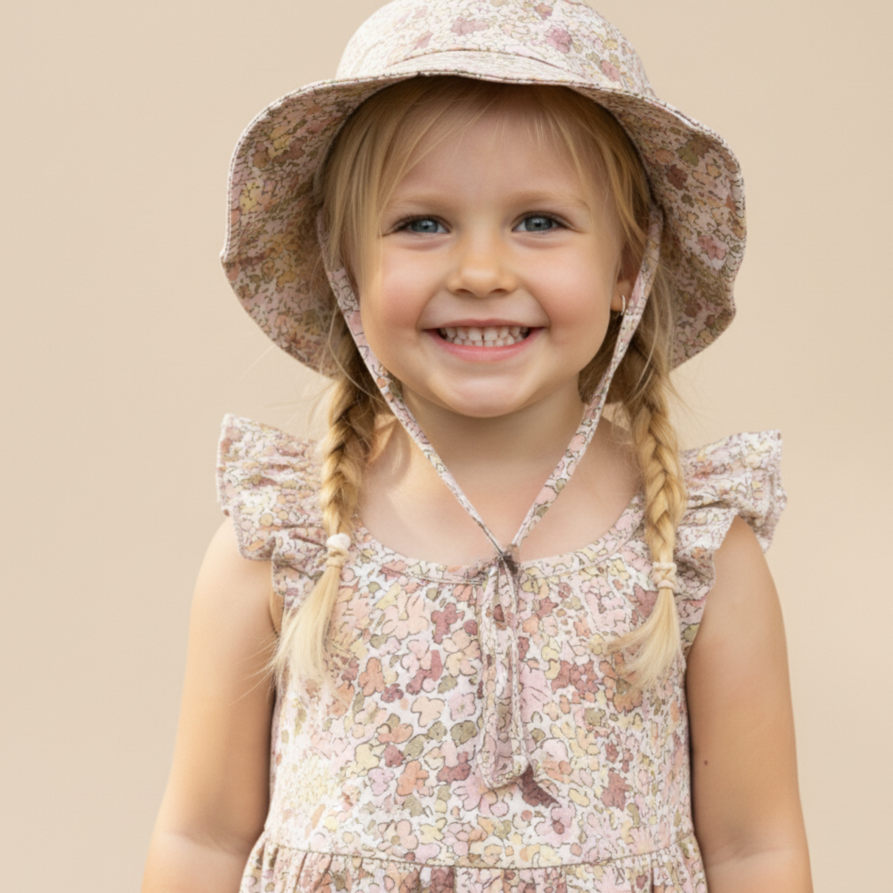 Young girl wearing a floral hat and dress against a beige background