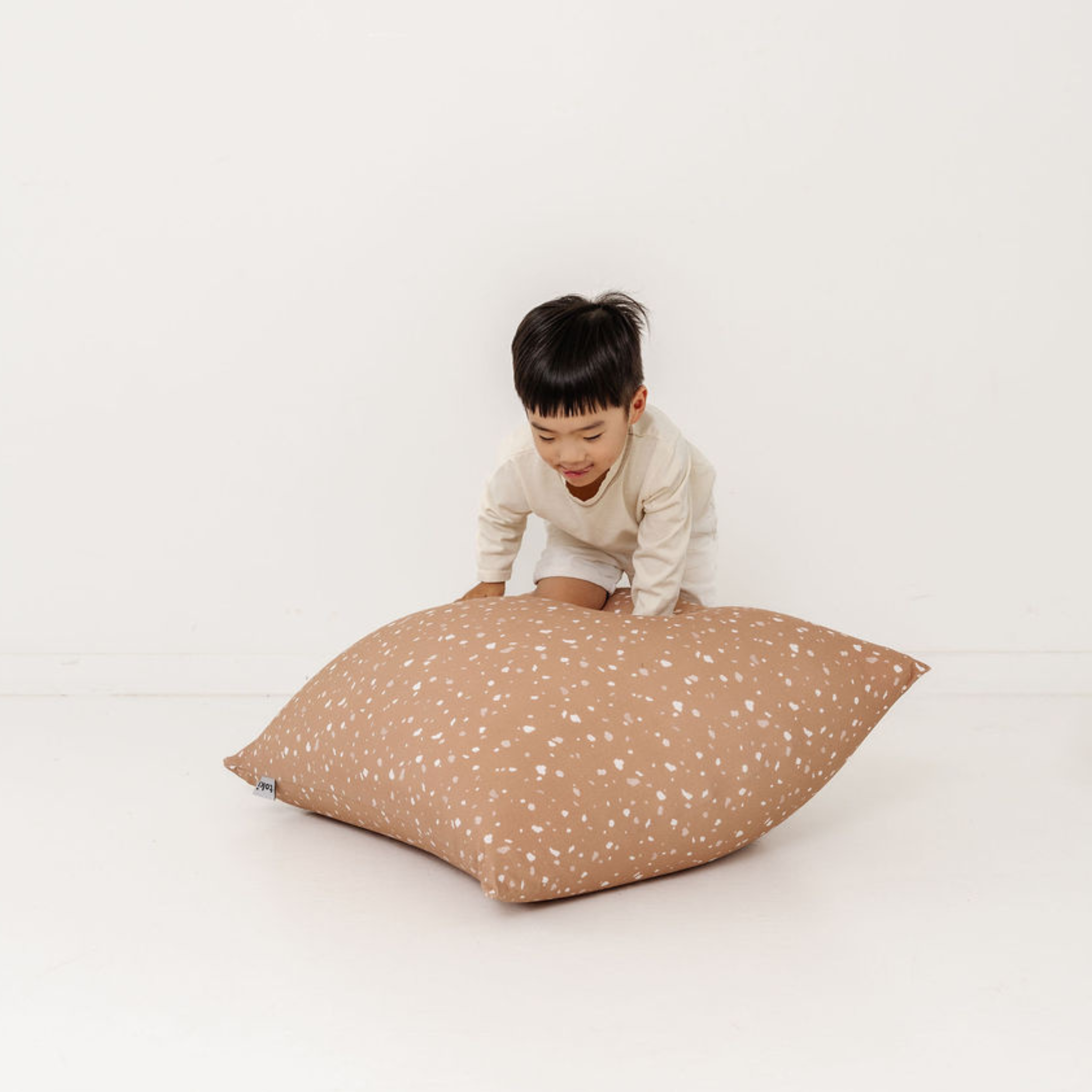Child playing with a large brown pillow on a white background