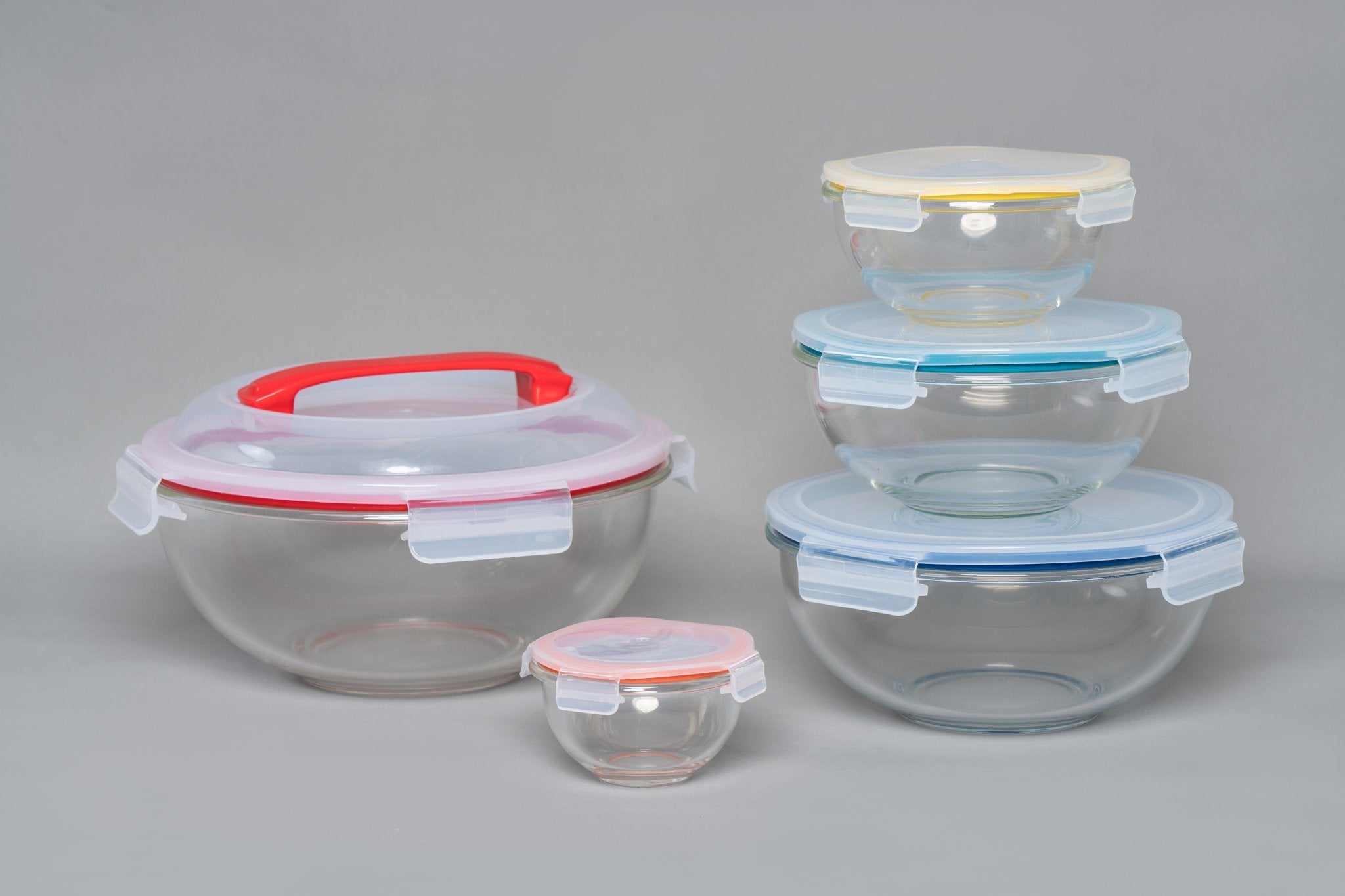 Set of glass food storage containers with colorful lids on a gray background