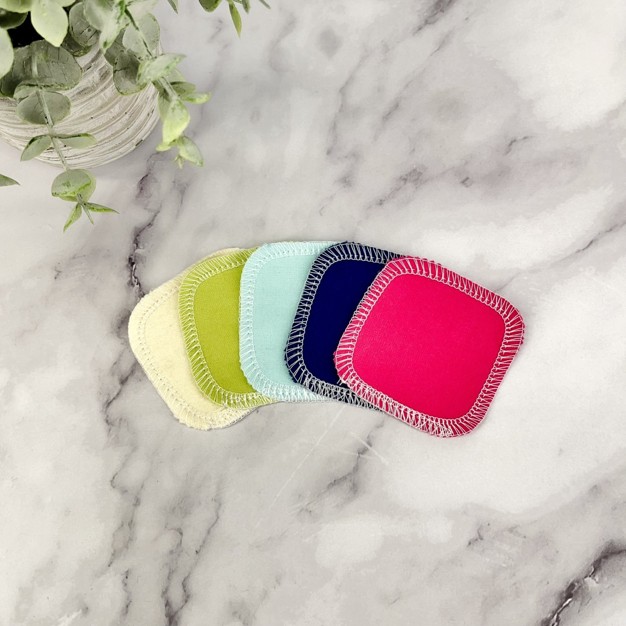 Set of colorful reusable pads on a marble surface with a plant in the background