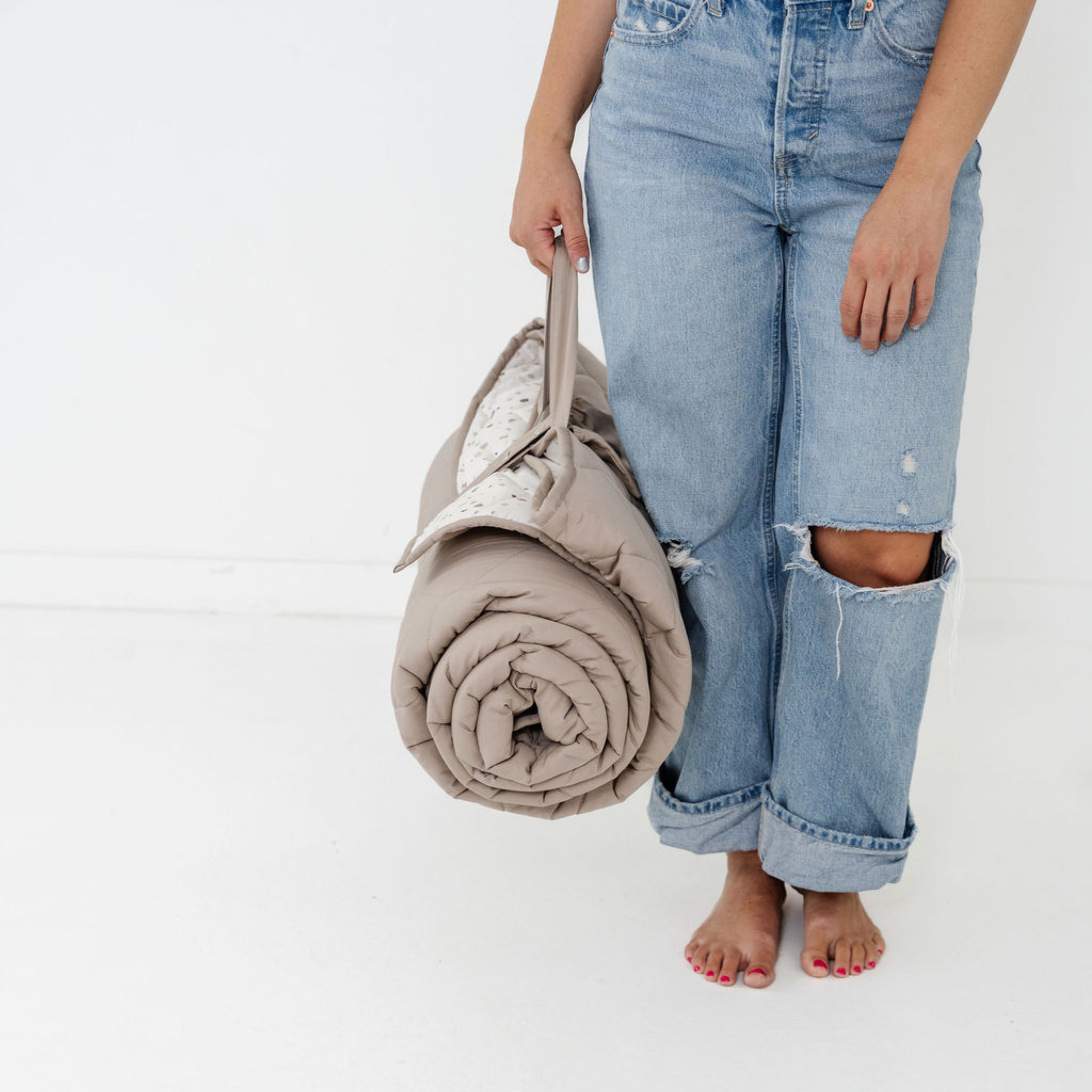 Person holding a beige blanket with ripped jeans on a white background