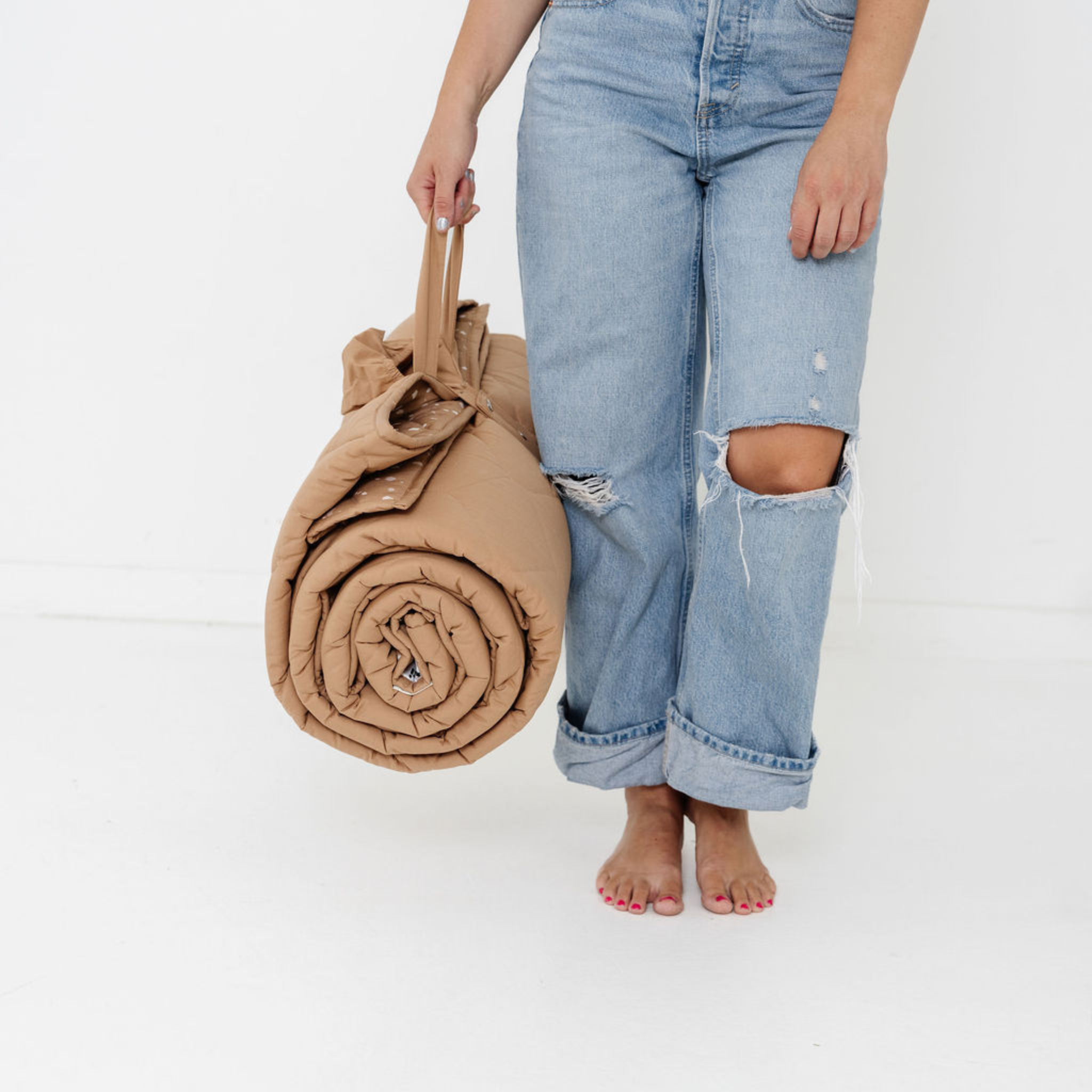 Person holding a rolled-up beige blanket wearing light blue jeans on a white background