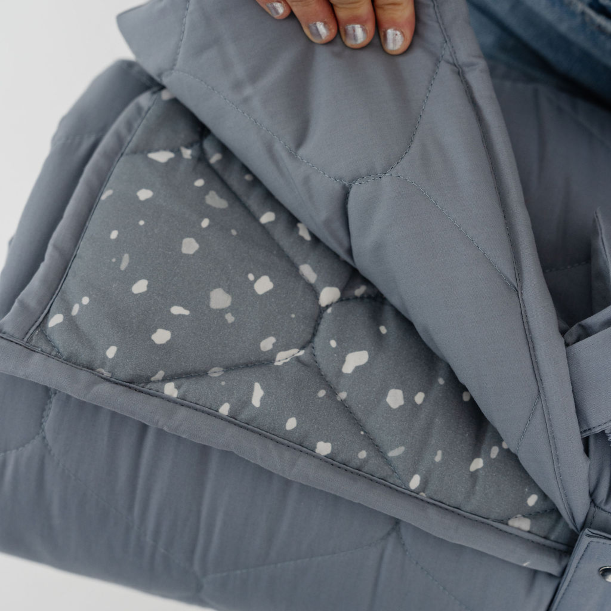 Gray quilted fabric with a terrazzo pattern held by a hand on a light gray background