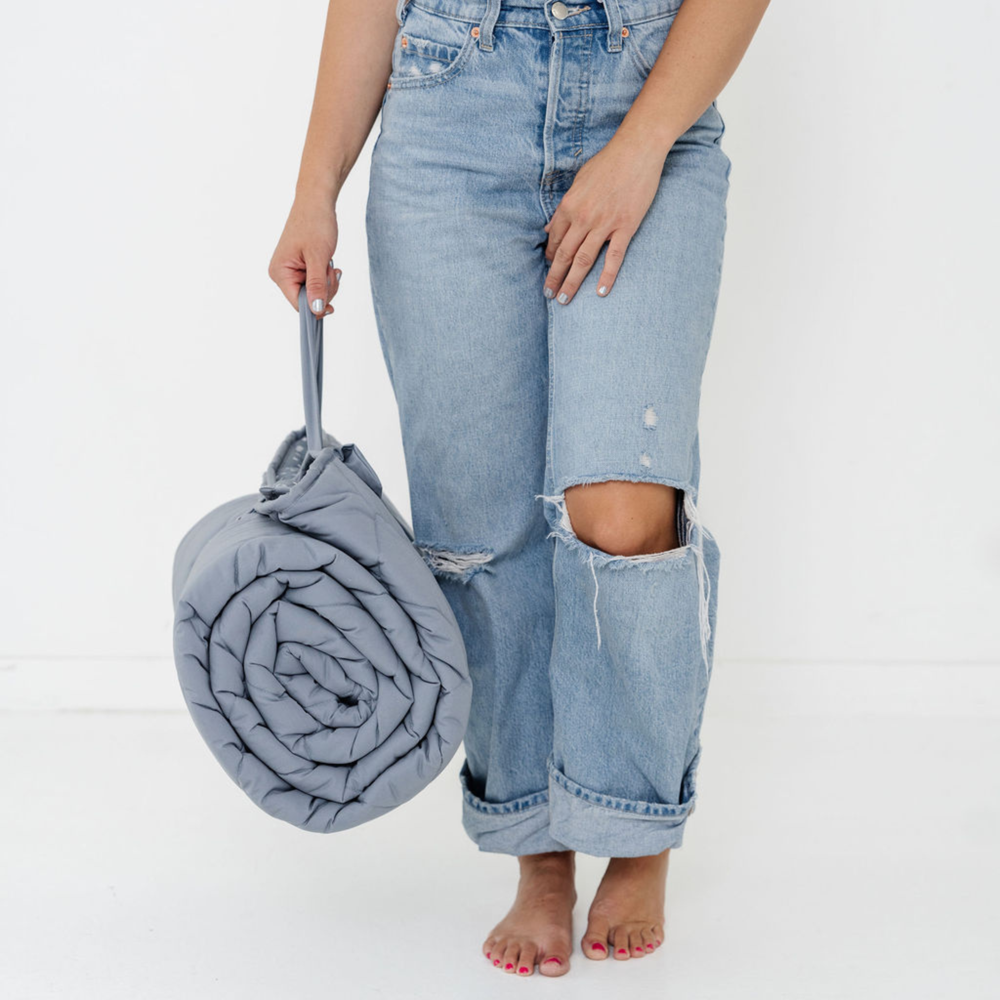 Person wearing light blue jeans holding a rolled-up blanket on a white background