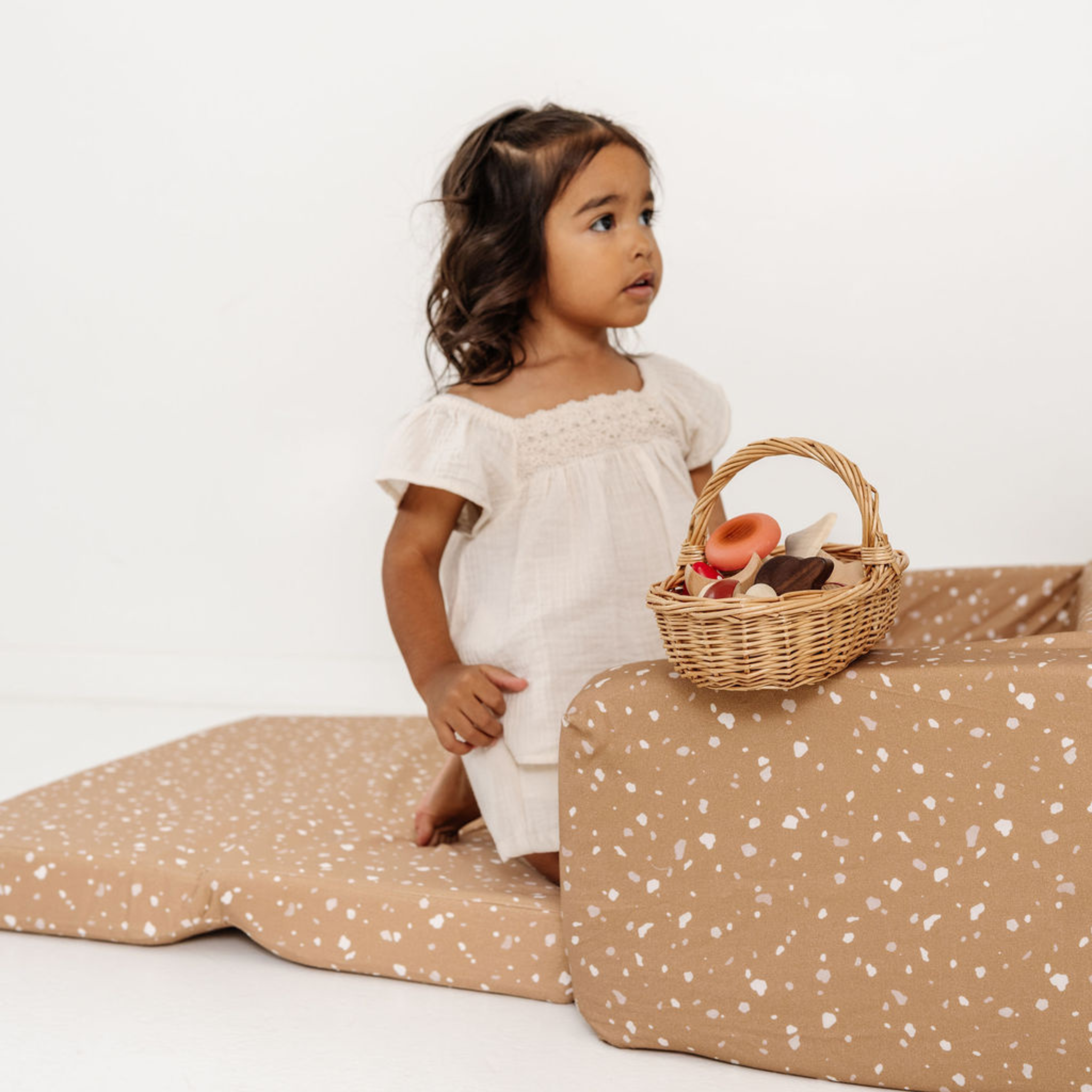 Child holding a wicker basket with toys on a beige and white polka dot surface.