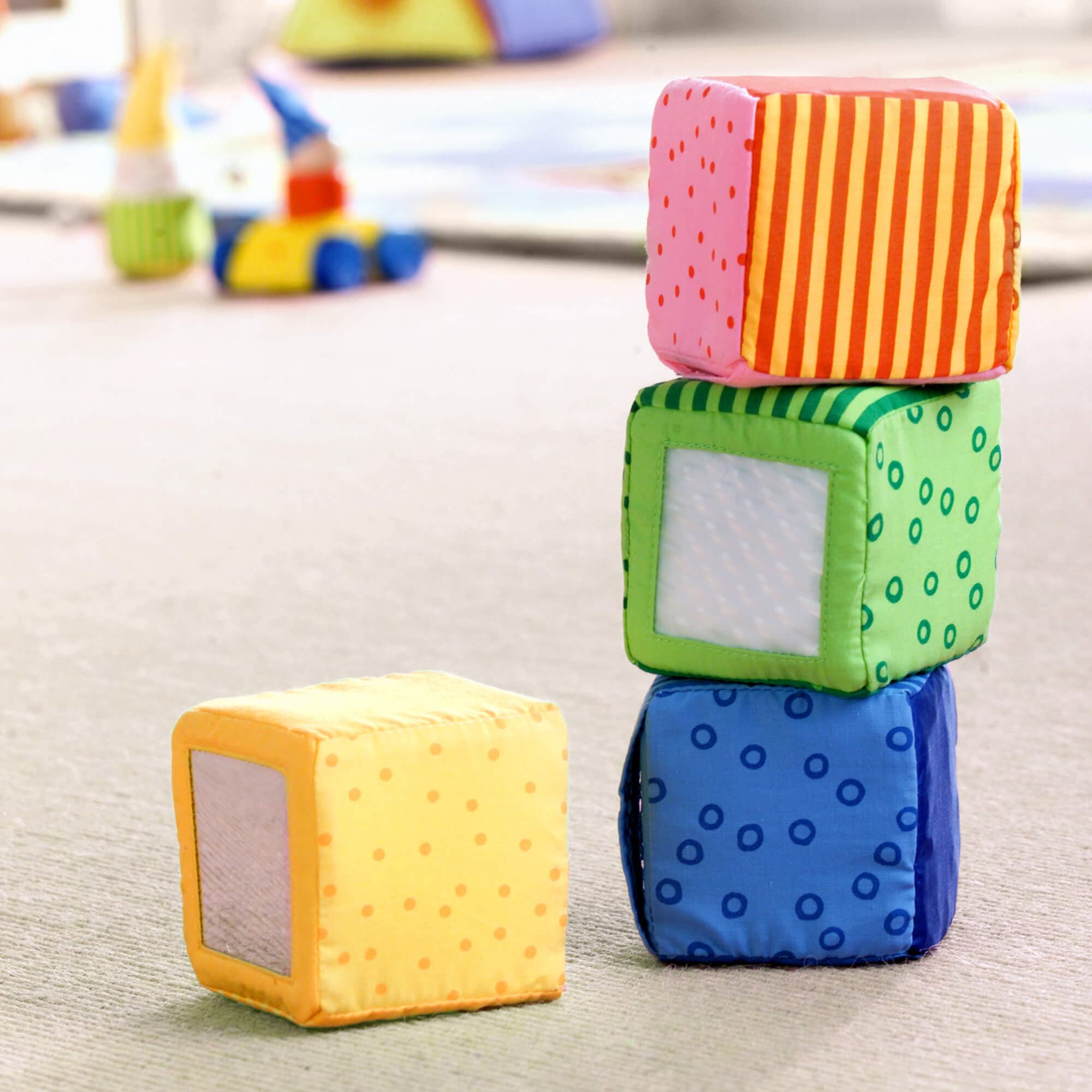 Colorful soft blocks stacked on a wooden floor with toys in the background