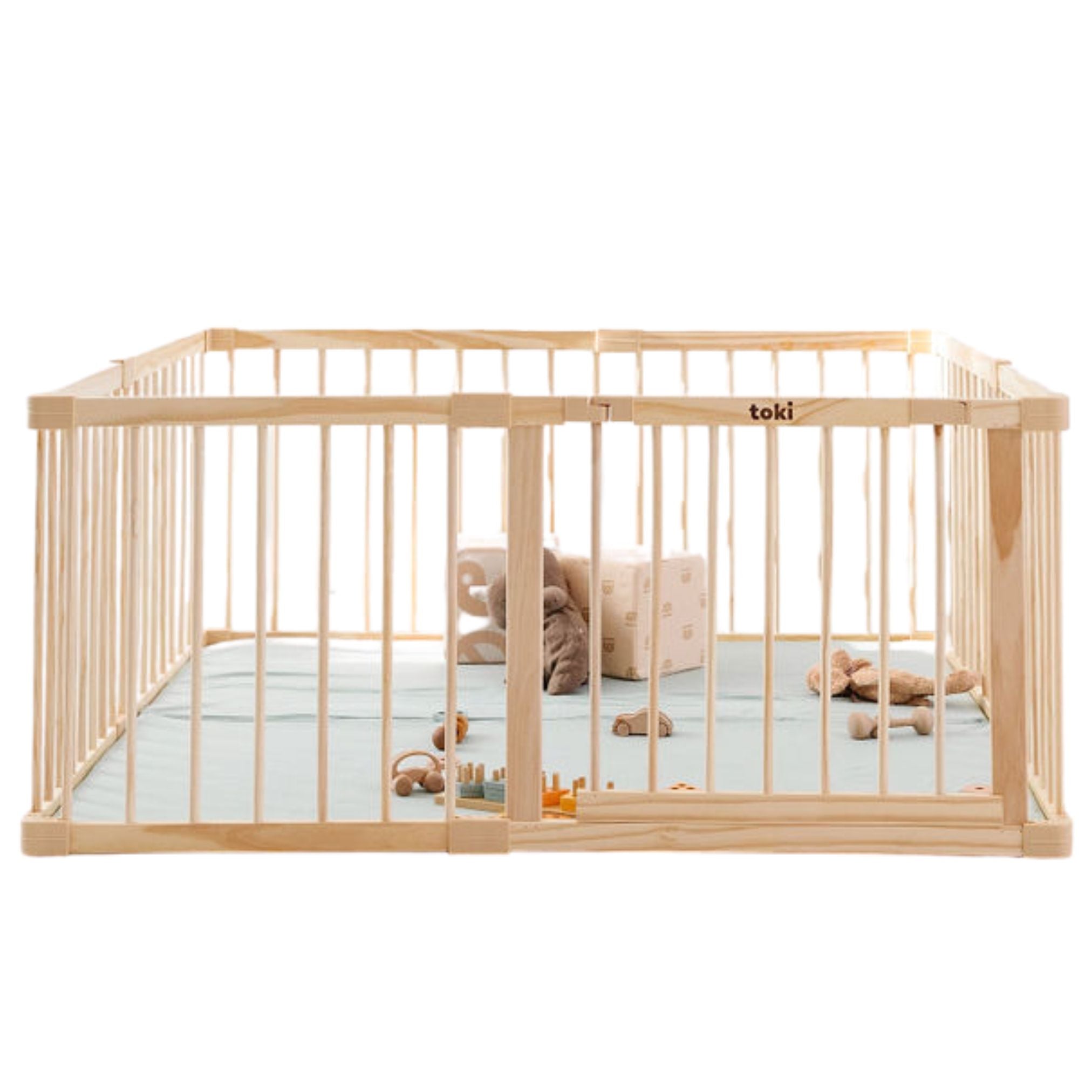 A light natural wood baby playpen with a light blue mattress and small toys inside, shown on a plain white background. The brand name 'toki' is visible on the upper rail.