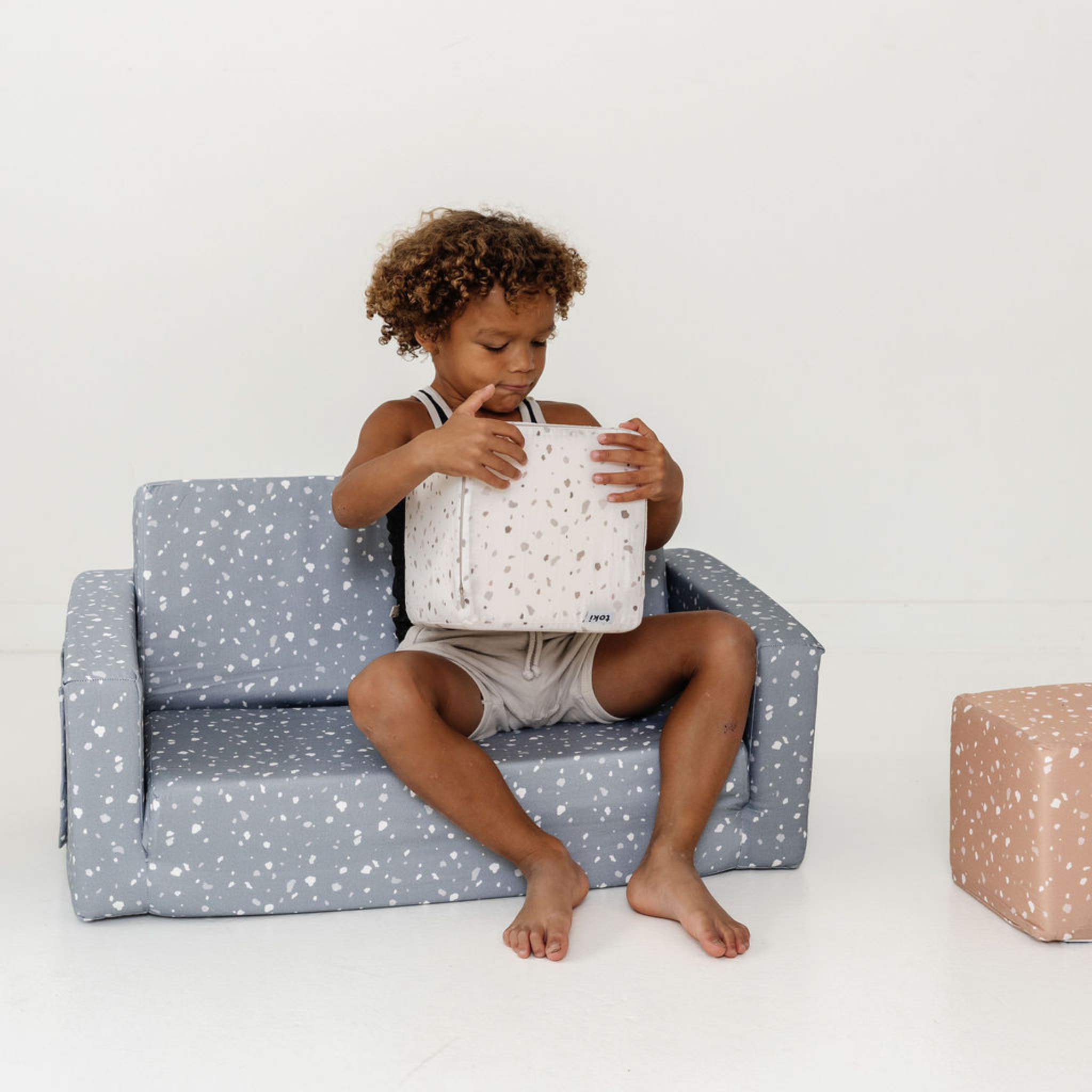 Child sitting on a star-patterned chair holding a matching bag against a white background