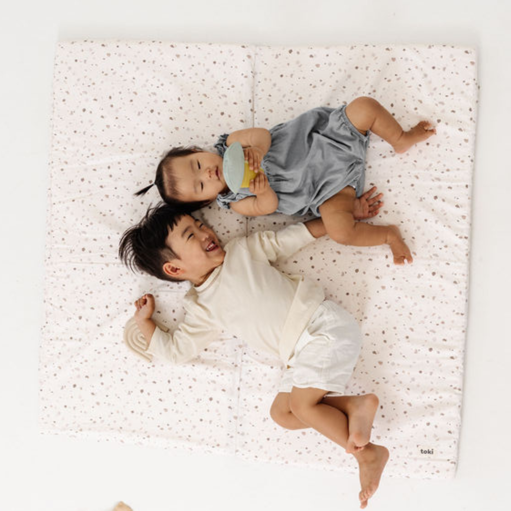 Two children lying on a white mattress with a polka dot pattern
