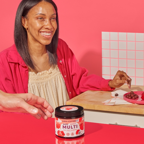 Woman in a kitchen setting with a jar of 'Multi' supplement on a red surface.