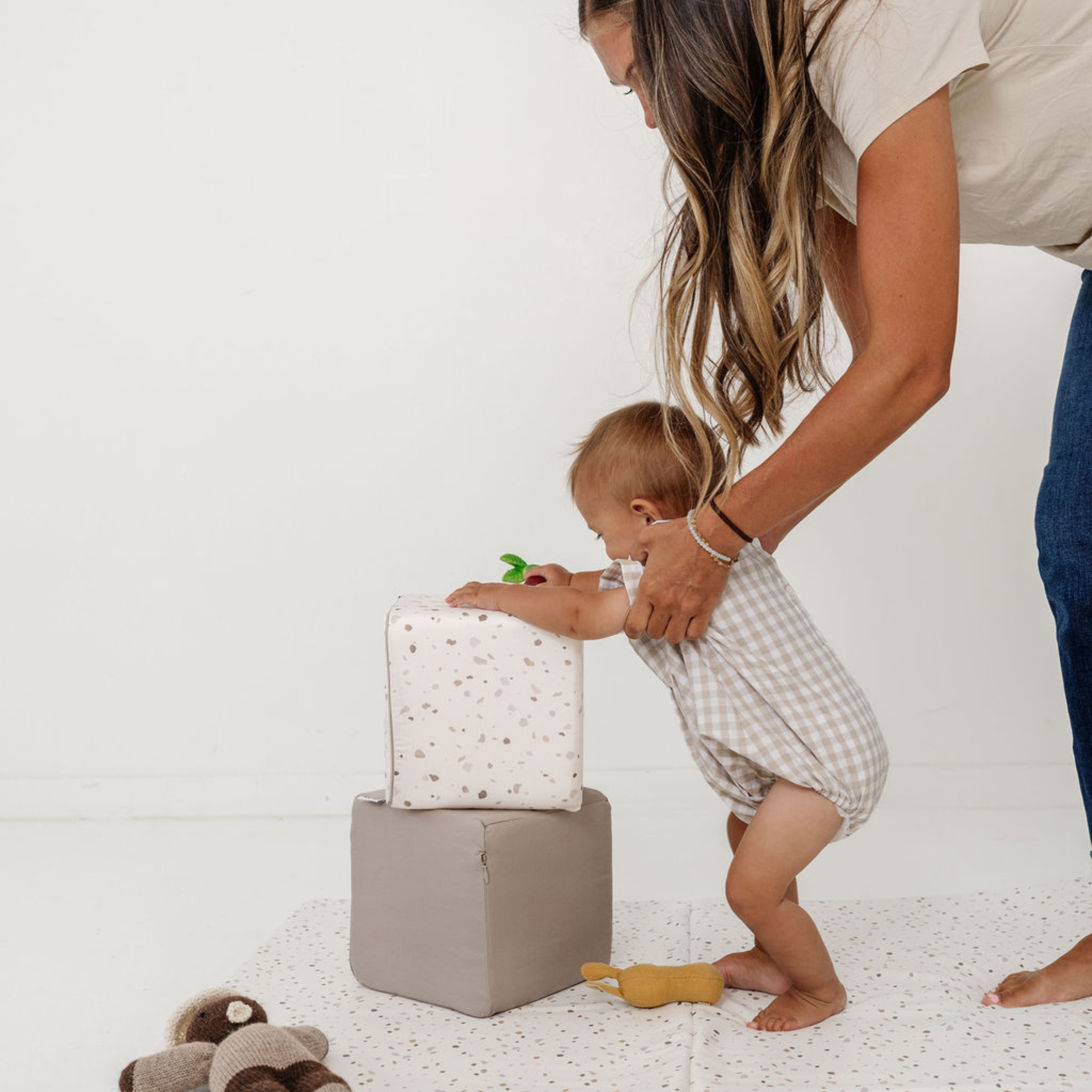 Woman assisting a baby on a soft surface with a white background